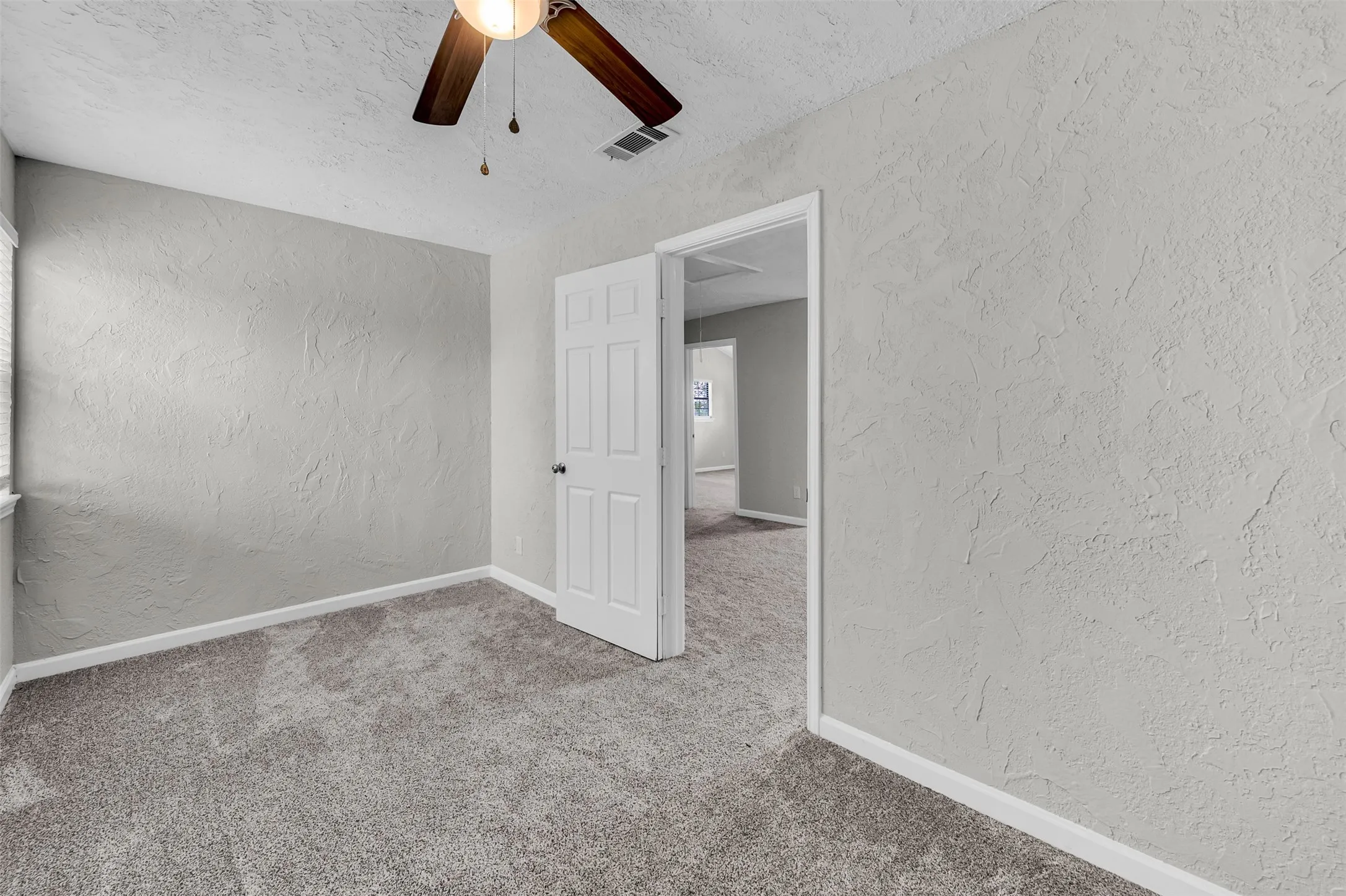 Unfurnished bedroom with a textured wall, carpet flooring, ceiling fan, and a textured ceiling