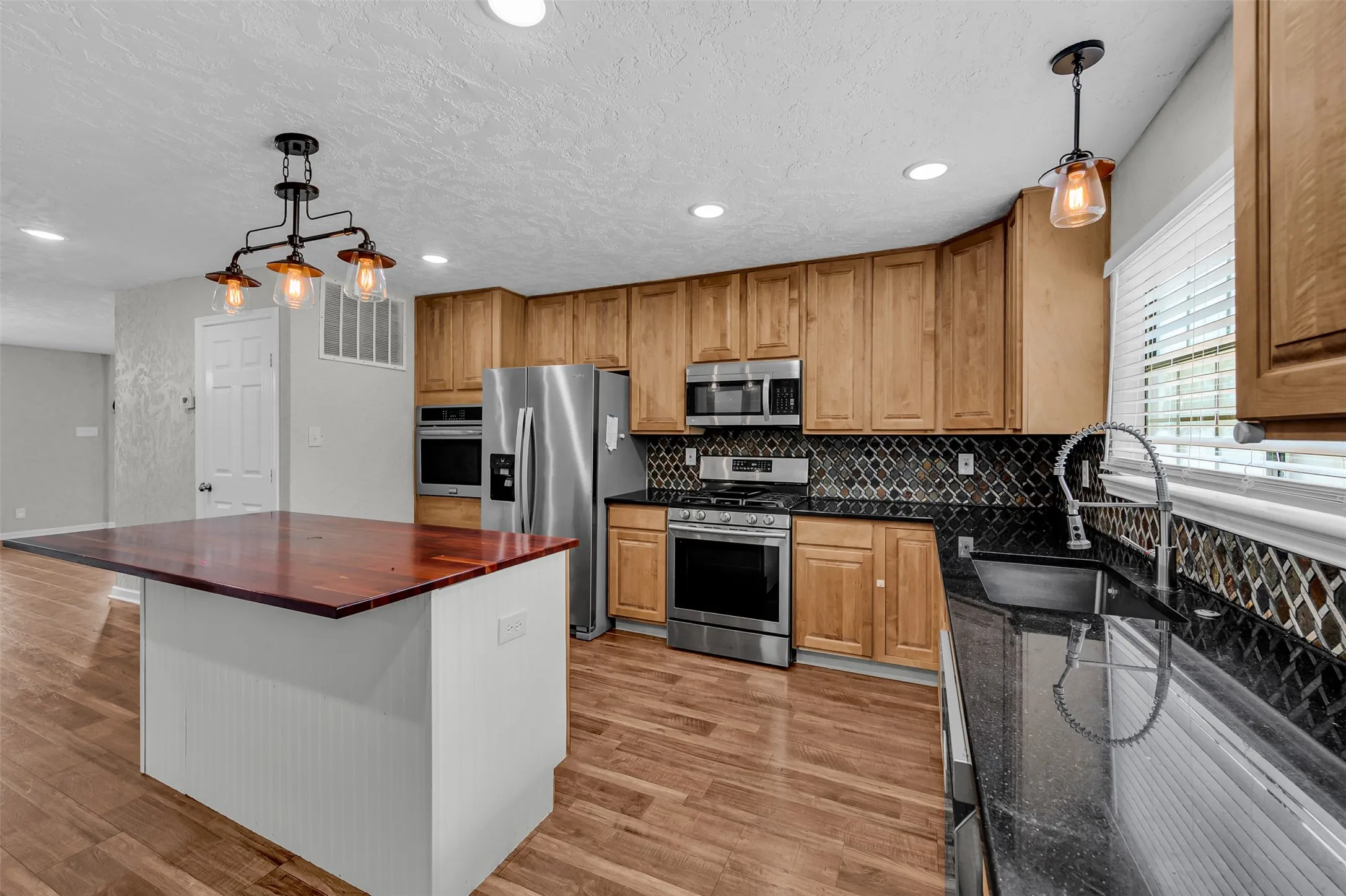 Kitchen featuring hanging light fixtures, recessed lighting, backsplash, stainless steel appliances, and light wood-style flooring
