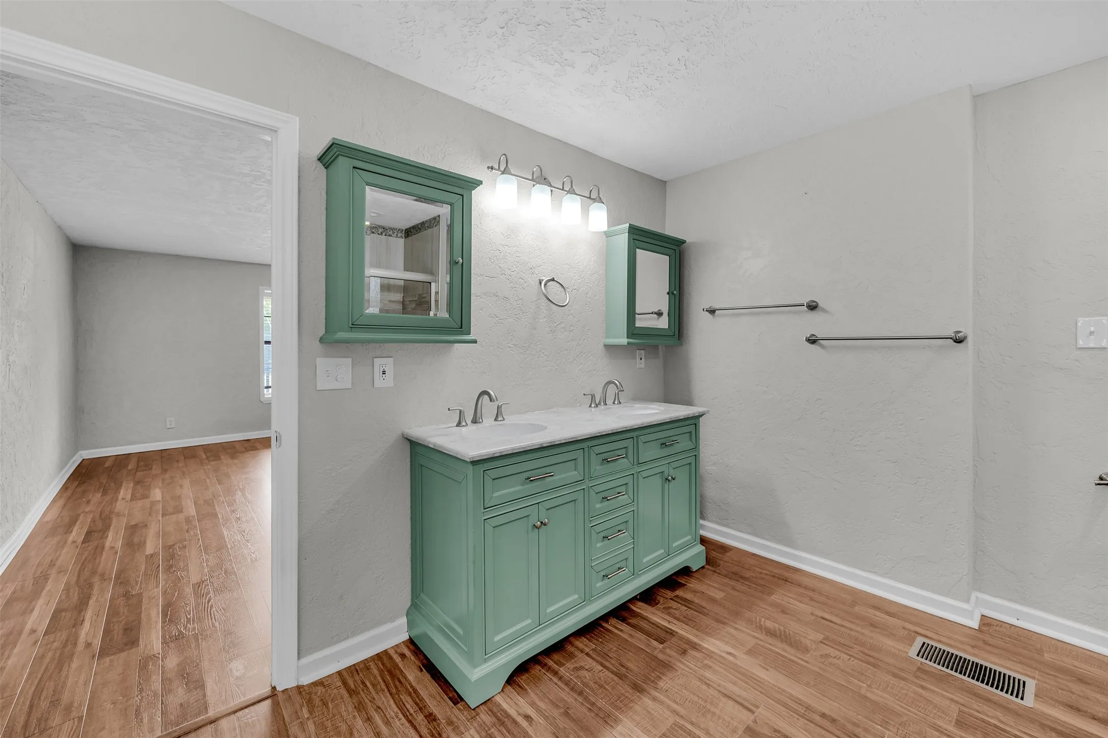 Bathroom with a textured ceiling, a textured wall, light wood-style flooring, and double vanity