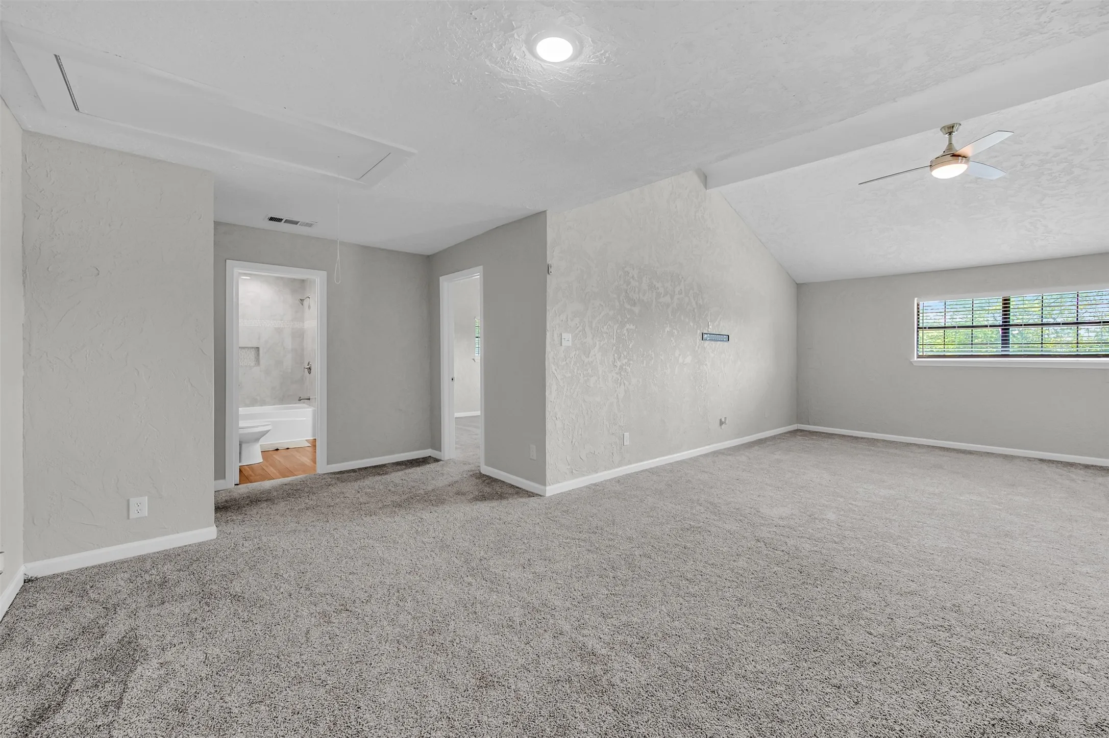 Empty room with a textured ceiling, lofted ceiling, a textured wall, light carpet, and ceiling fan