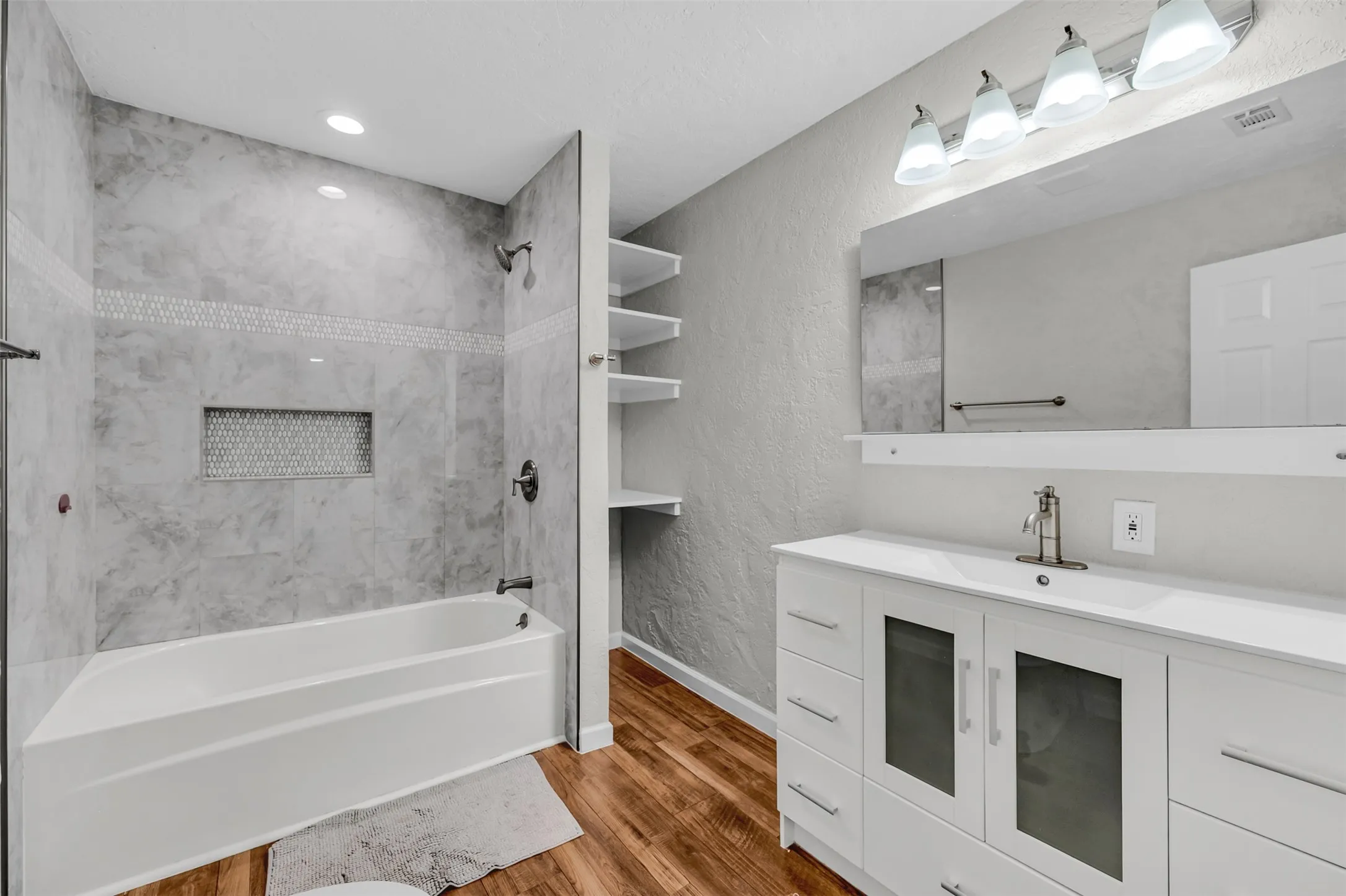 Bathroom featuring a textured wall, bathtub / shower combination, vanity, and dark wood-style floors