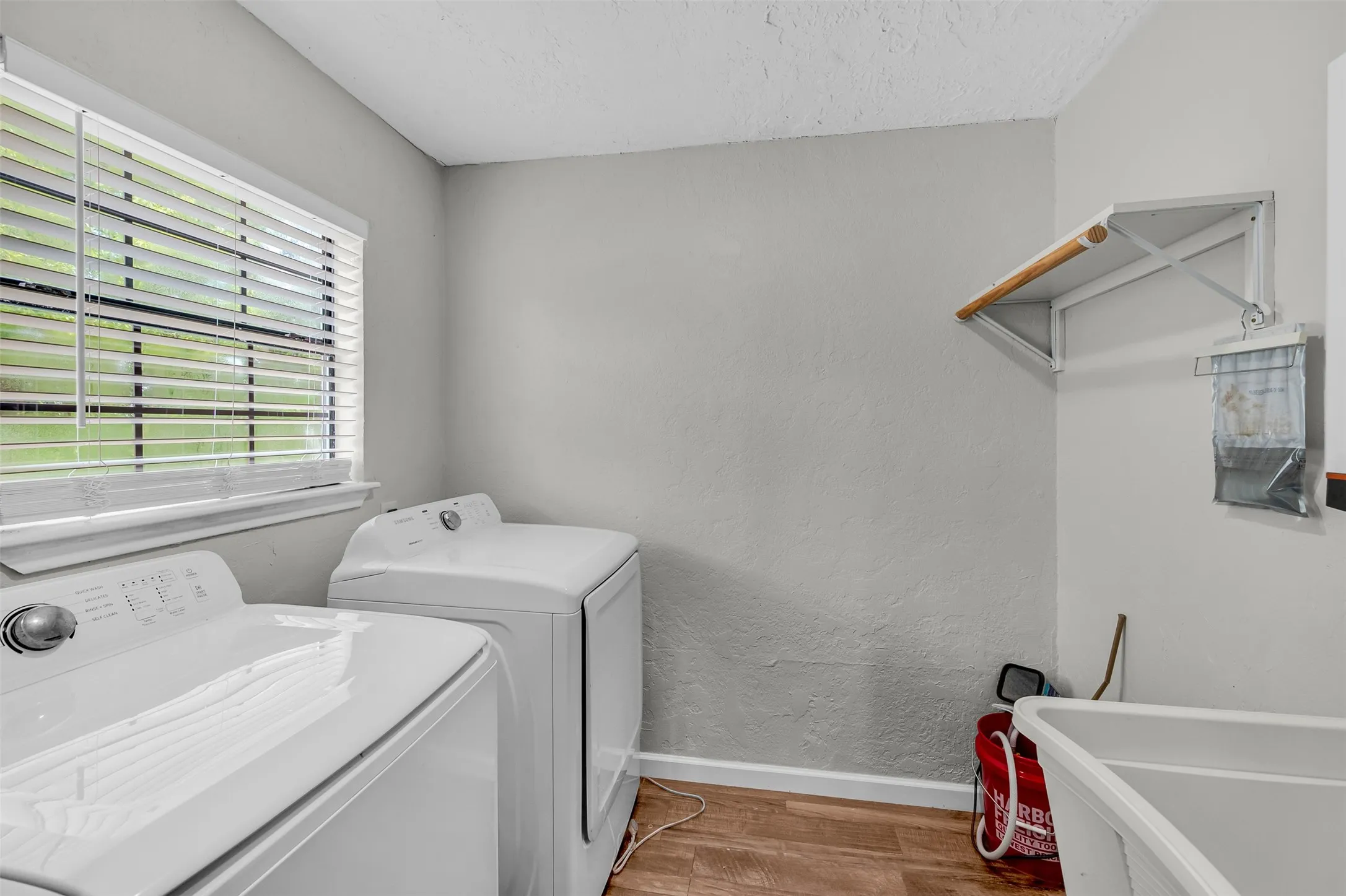 Laundry room featuring light wood-style flooring, a textured ceiling, washing machine and dryer, and a textured wall