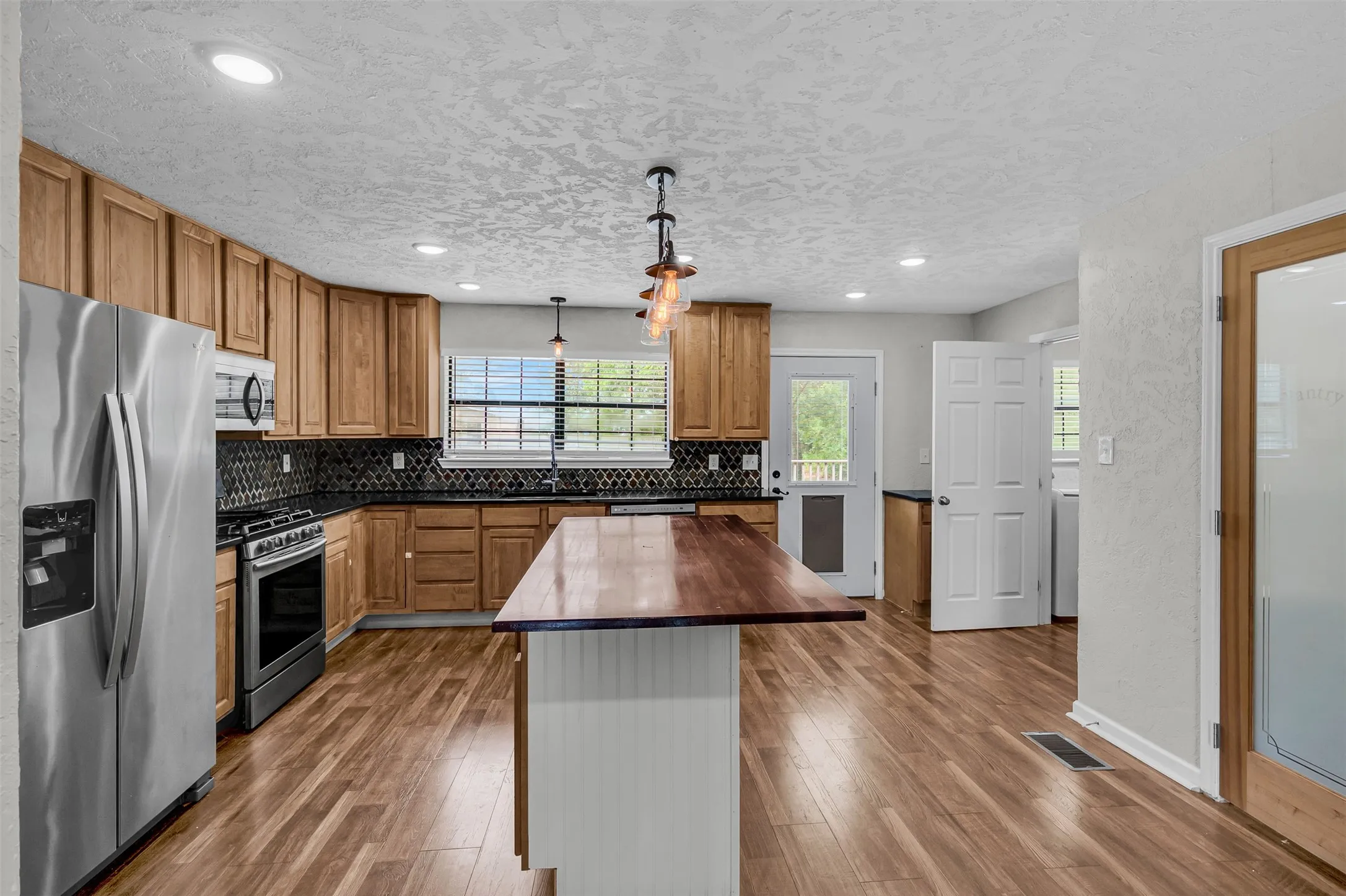 Kitchen featuring stainless steel appliances, decorative light fixtures, wood counters, decorative backsplash, and dark wood-style floors
