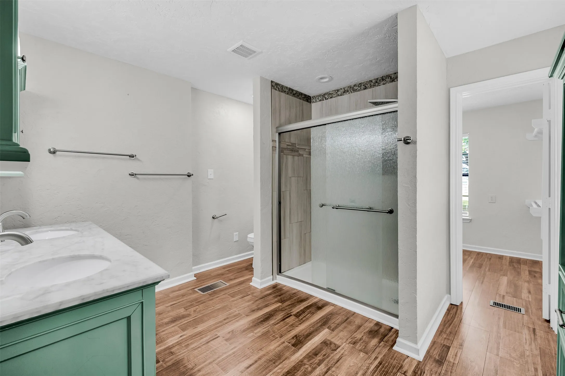 Bathroom featuring a stall shower, light wood-style floors, double vanity, and a textured ceiling