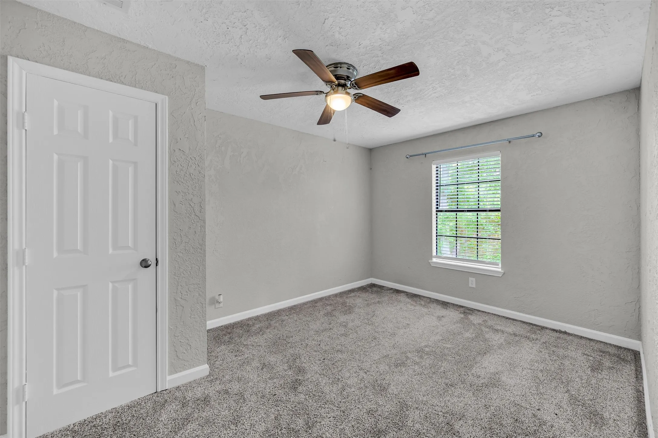 Spare room with a textured wall, a textured ceiling, light carpet, and ceiling fan