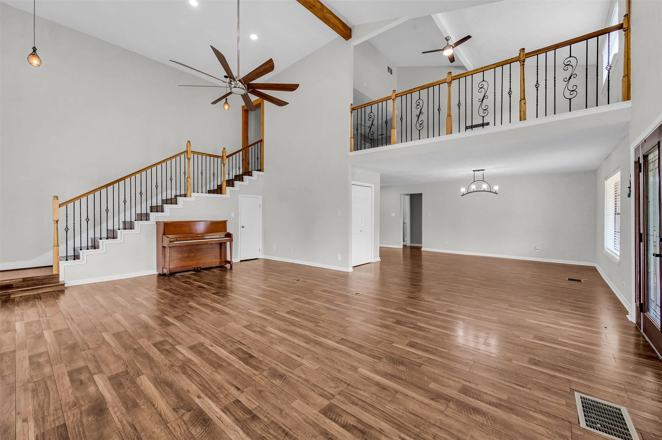 Unfurnished living room featuring a ceiling fan, beamed ceiling, wood finished floors, high vaulted ceiling, and stairs