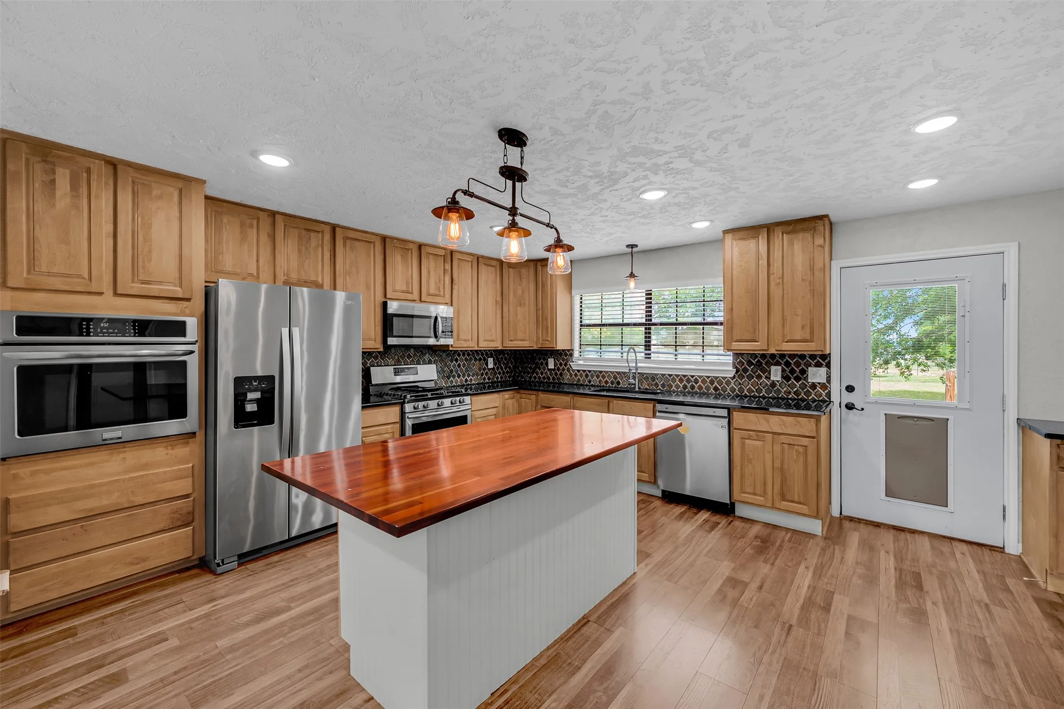 Kitchen with appliances with stainless steel finishes, pendant lighting, tasteful backsplash, light wood-type flooring, and recessed lighting