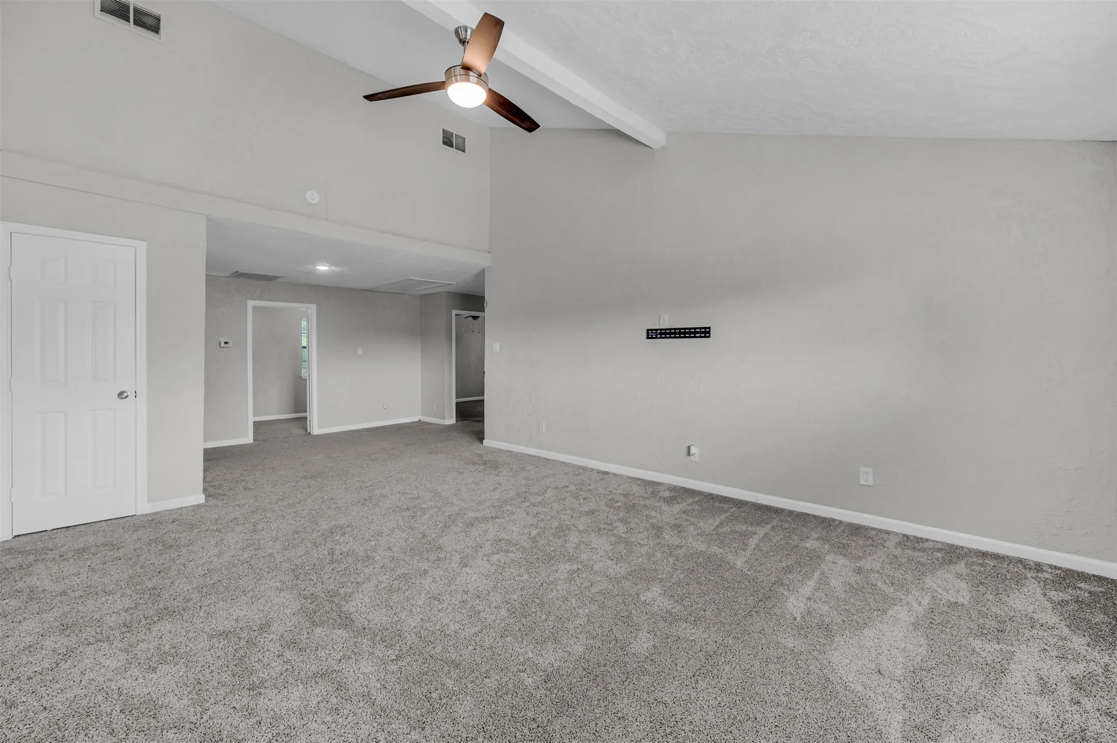 Empty room with light carpet, beam ceiling, ceiling fan, and high vaulted ceiling