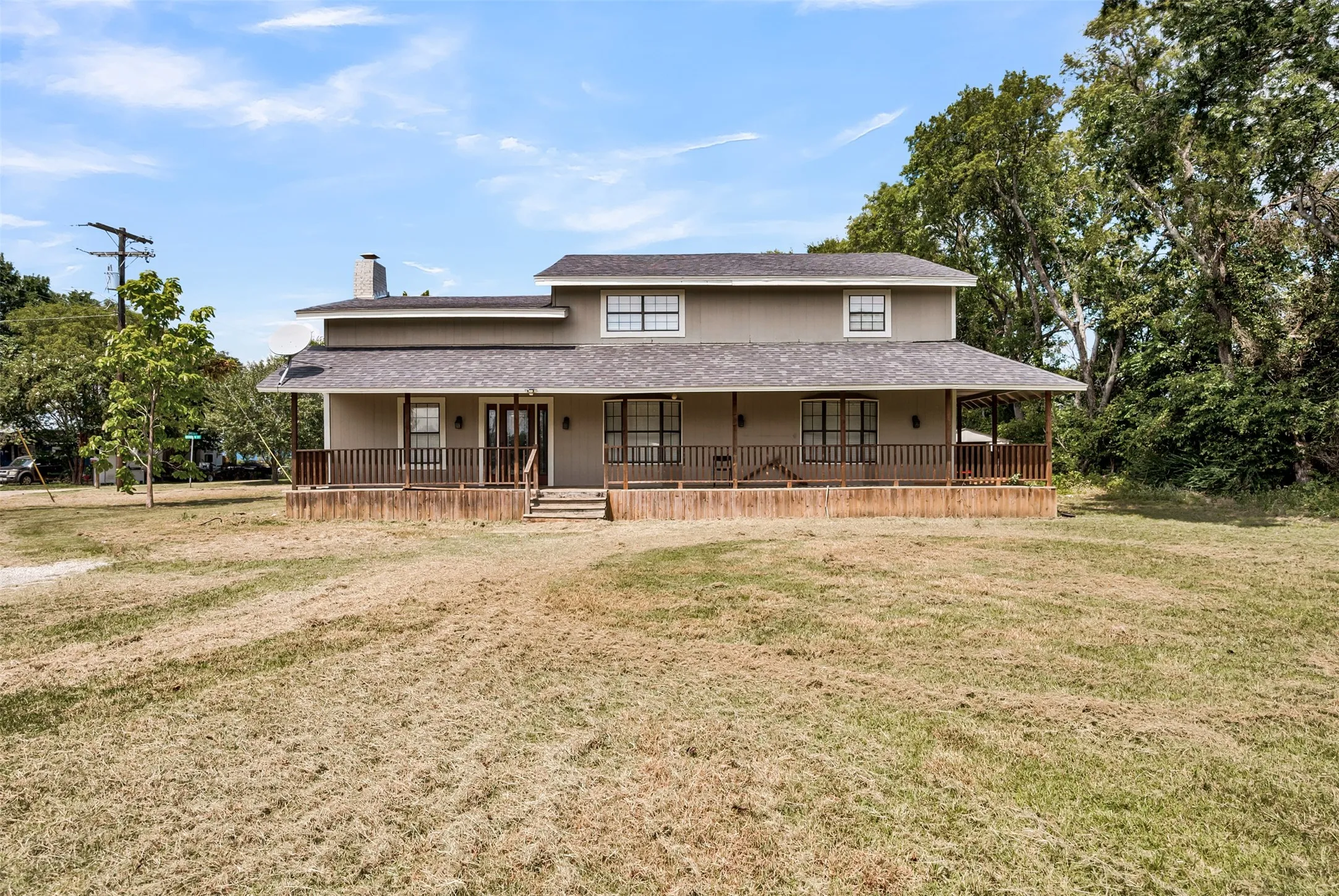 Farmhouse-style home with a porch, a chimney, a front yard, a shingled roof, and dirt driveway