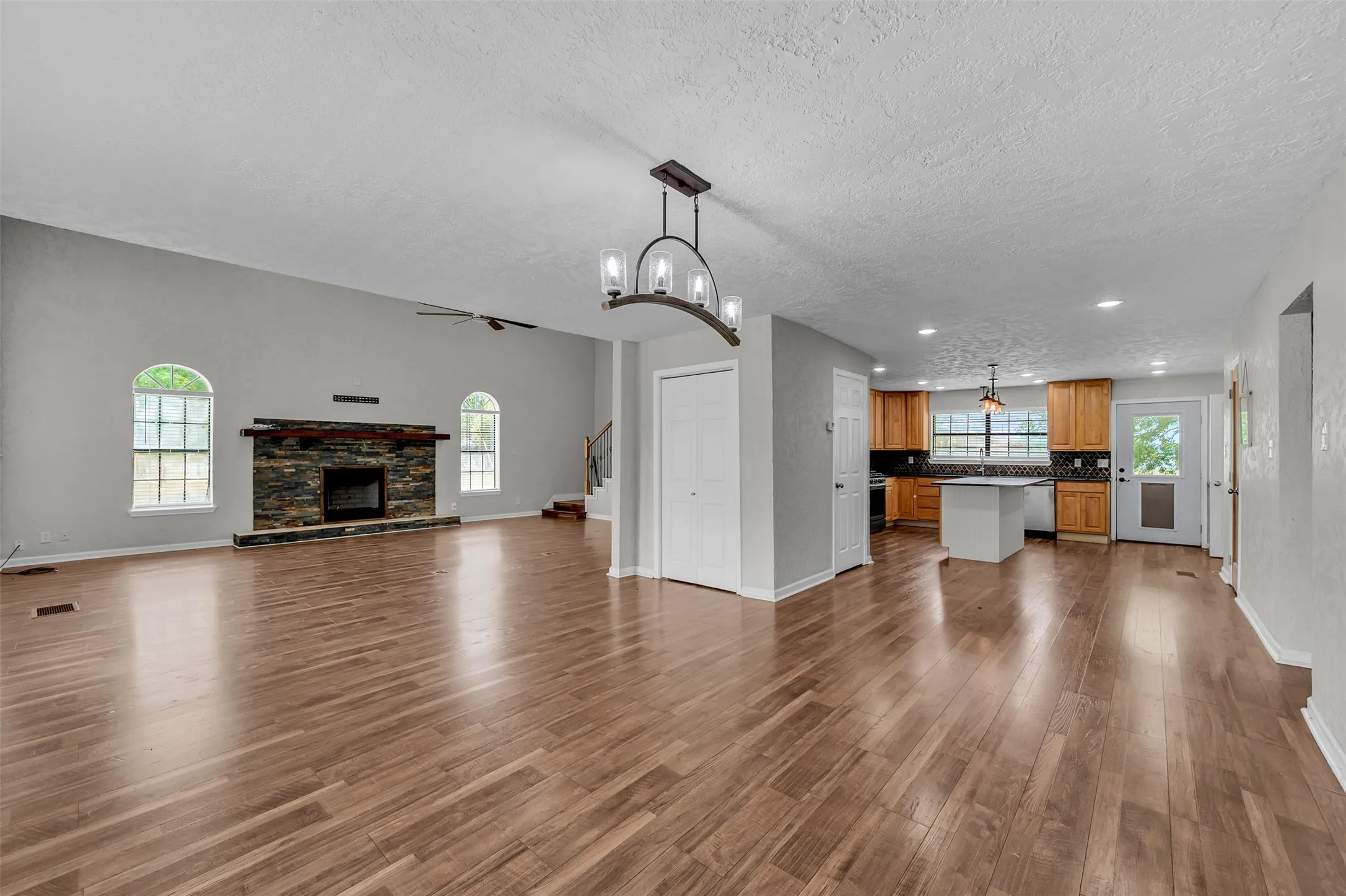 Unfurnished living room with dark wood finished floors, a fireplace, stairs, a chandelier, and a textured ceiling