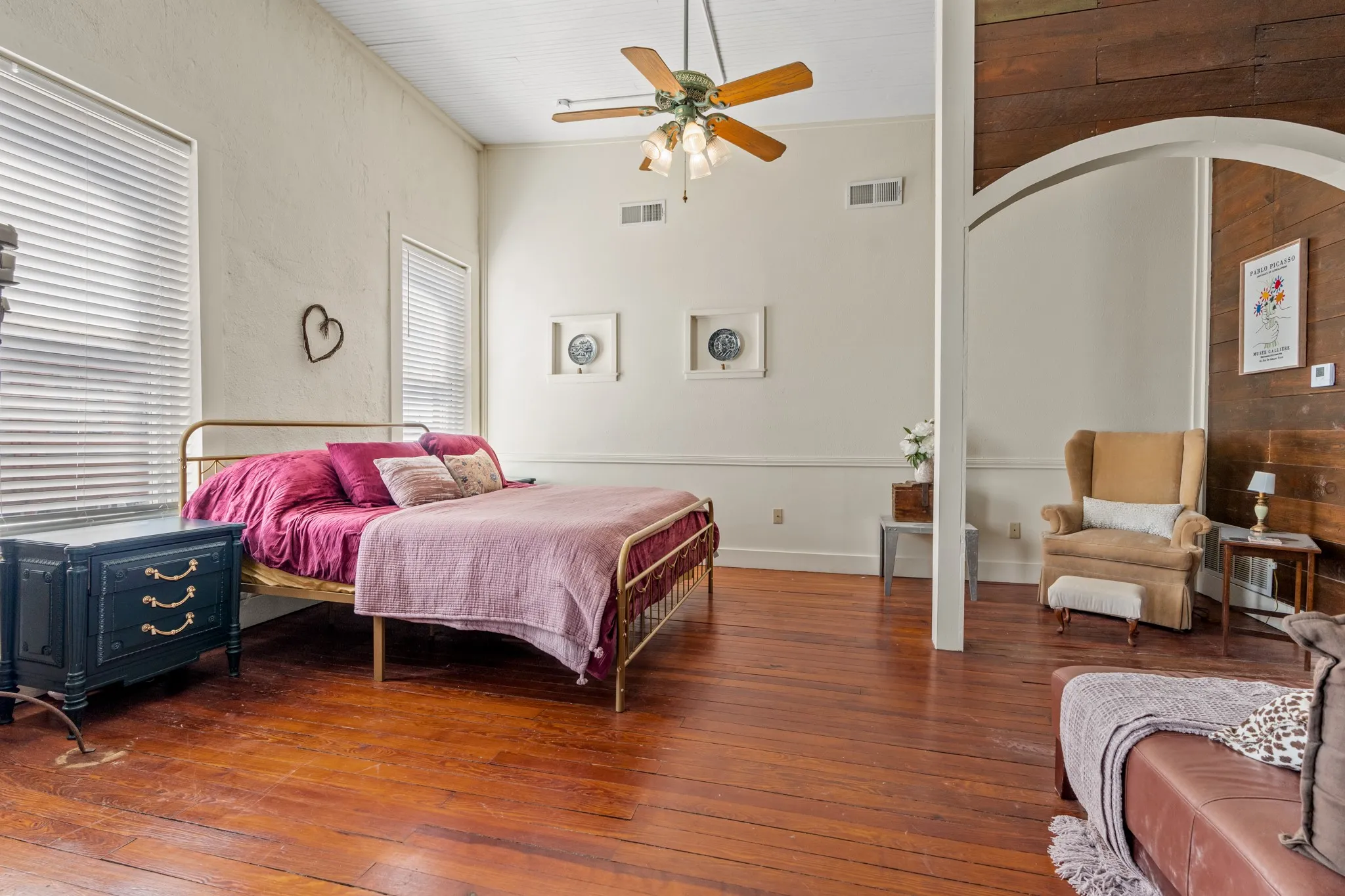 Bedroom with wood-type flooring, ceiling fan, high vaulted ceiling, and wood walls