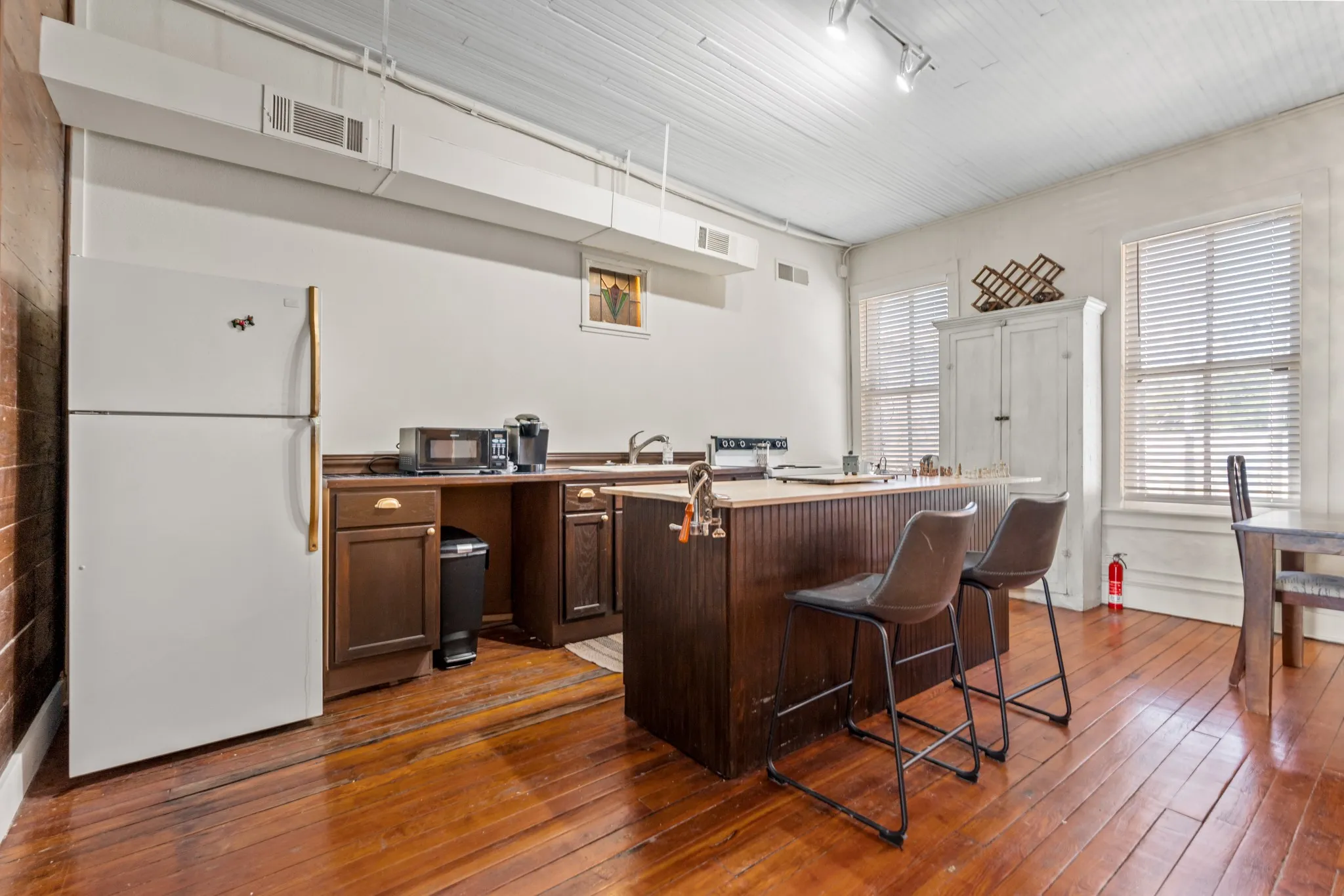 Kitchen with freestanding refrigerator, dark wood-style floors, a kitchen breakfast bar, a kitchen island, and dark brown cabinets