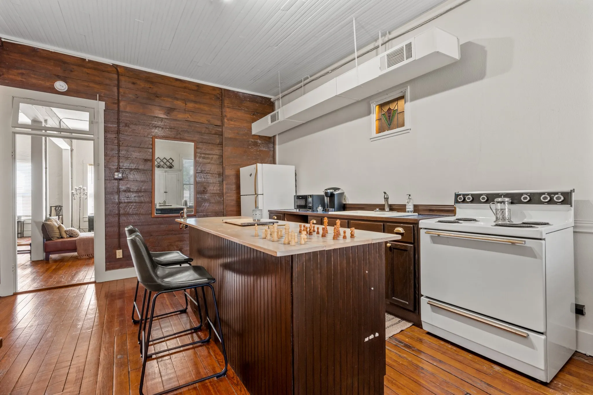 Kitchen with wood walls, white appliances, dark brown cabinets, dark wood-style floors, and a kitchen bar