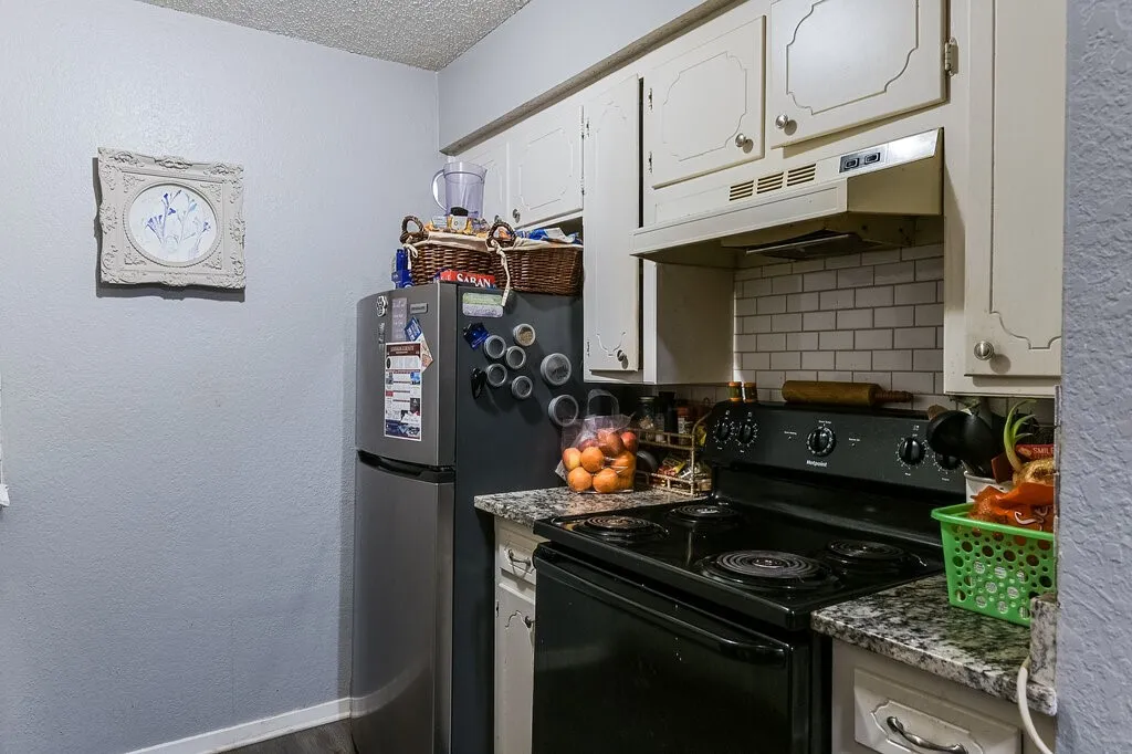 Right Unit Kitchen with black electric range oven, a textured wall, backsplash, under cabinet range hood, and white cabinets