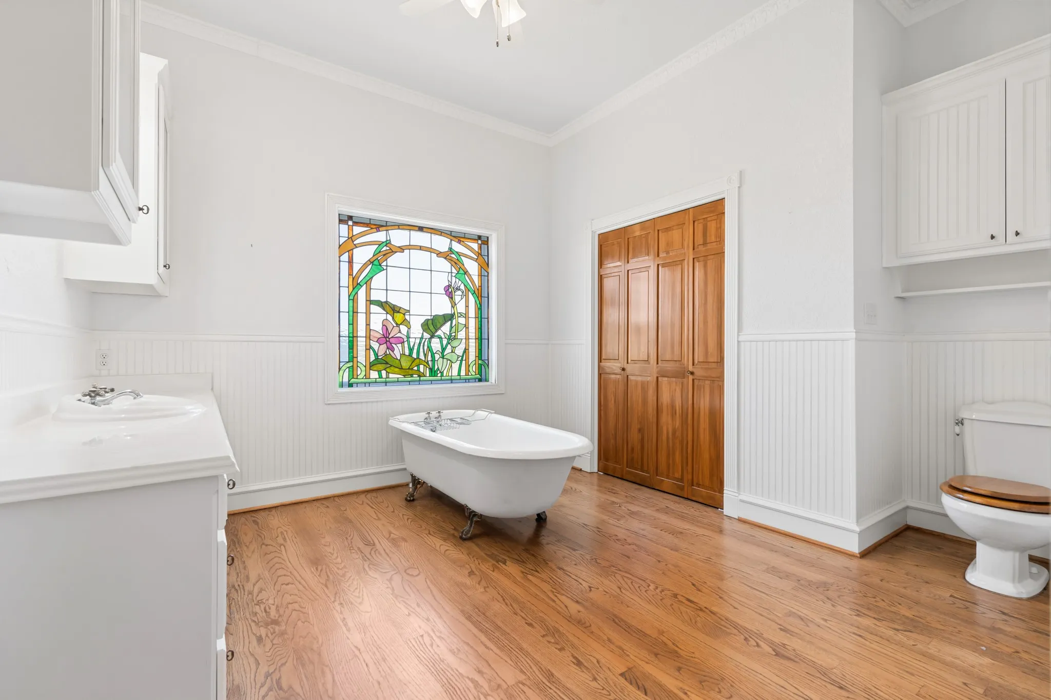 Bathroom with a freestanding tub, light wood-style floors, ornamental molding, vanity, and wainscoting