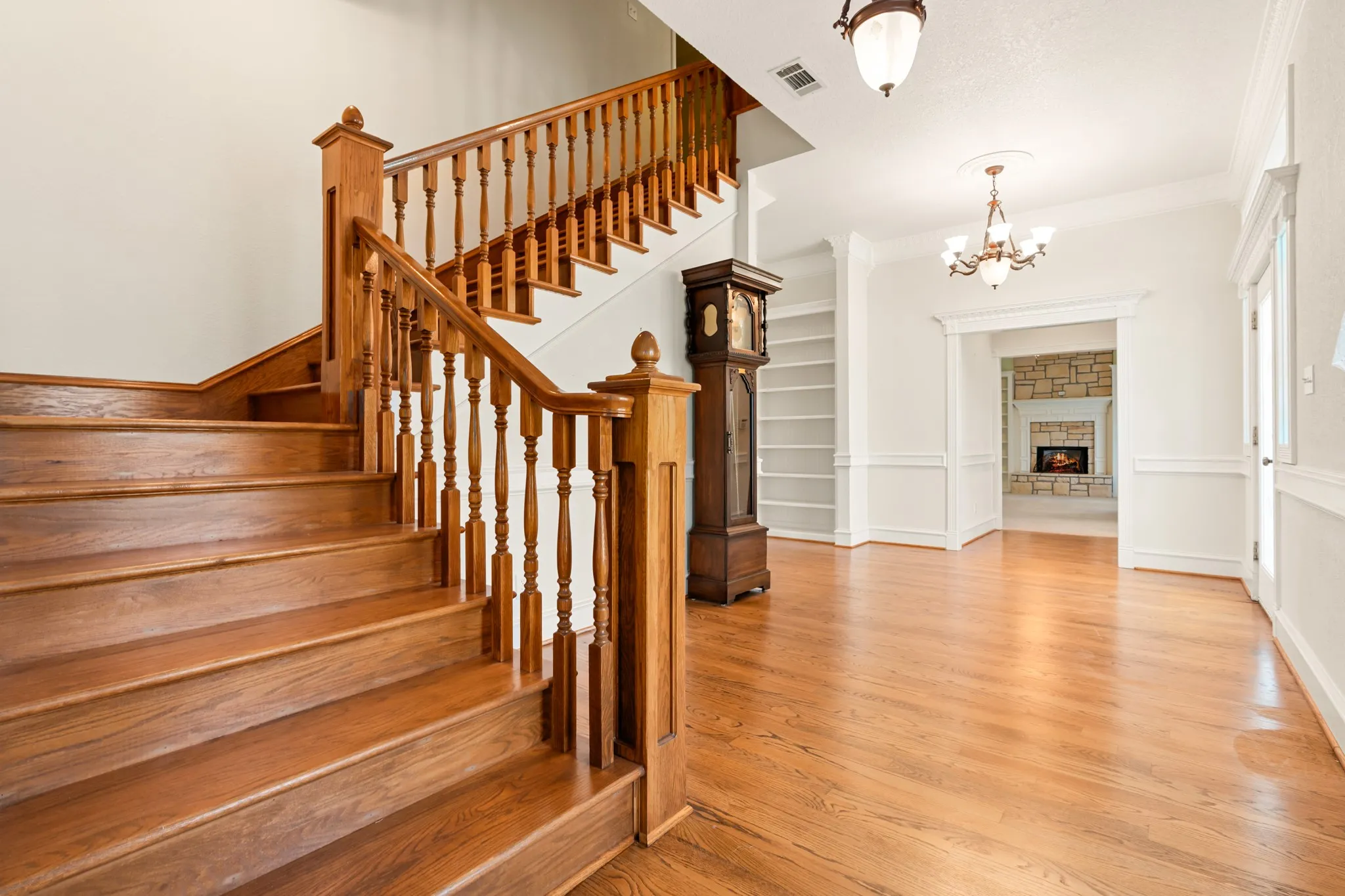 Staircase with a fireplace, wood finished floors, ornamental molding, and a chandelier