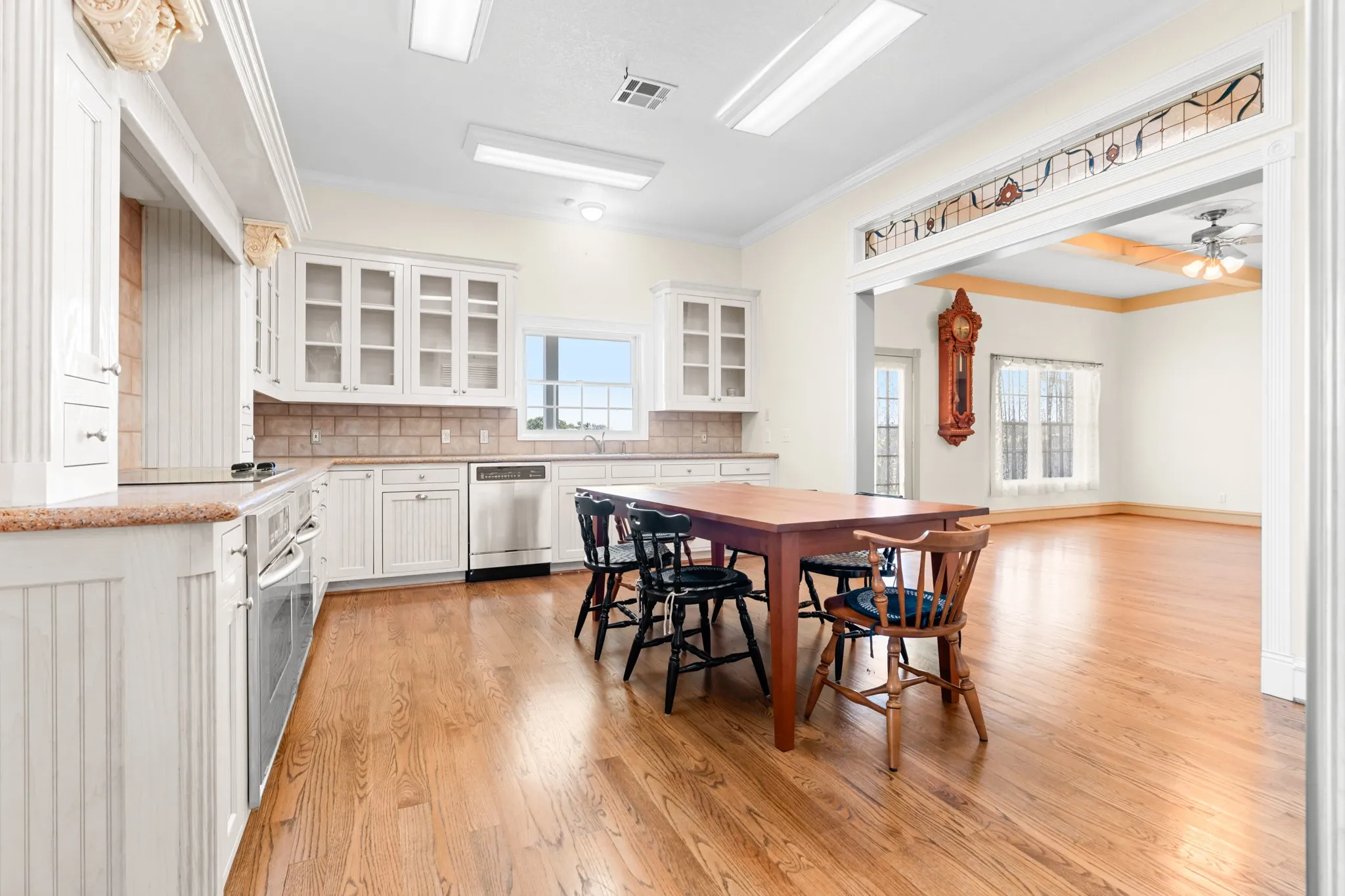 Kitchen featuring glass insert cabinets, tasteful backsplash, white cabinets, light wood-type flooring, and crown molding