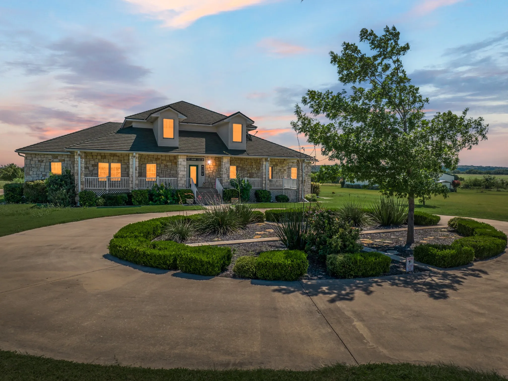 View of front of house with stone siding, a front yard, a porch, and curved driveway