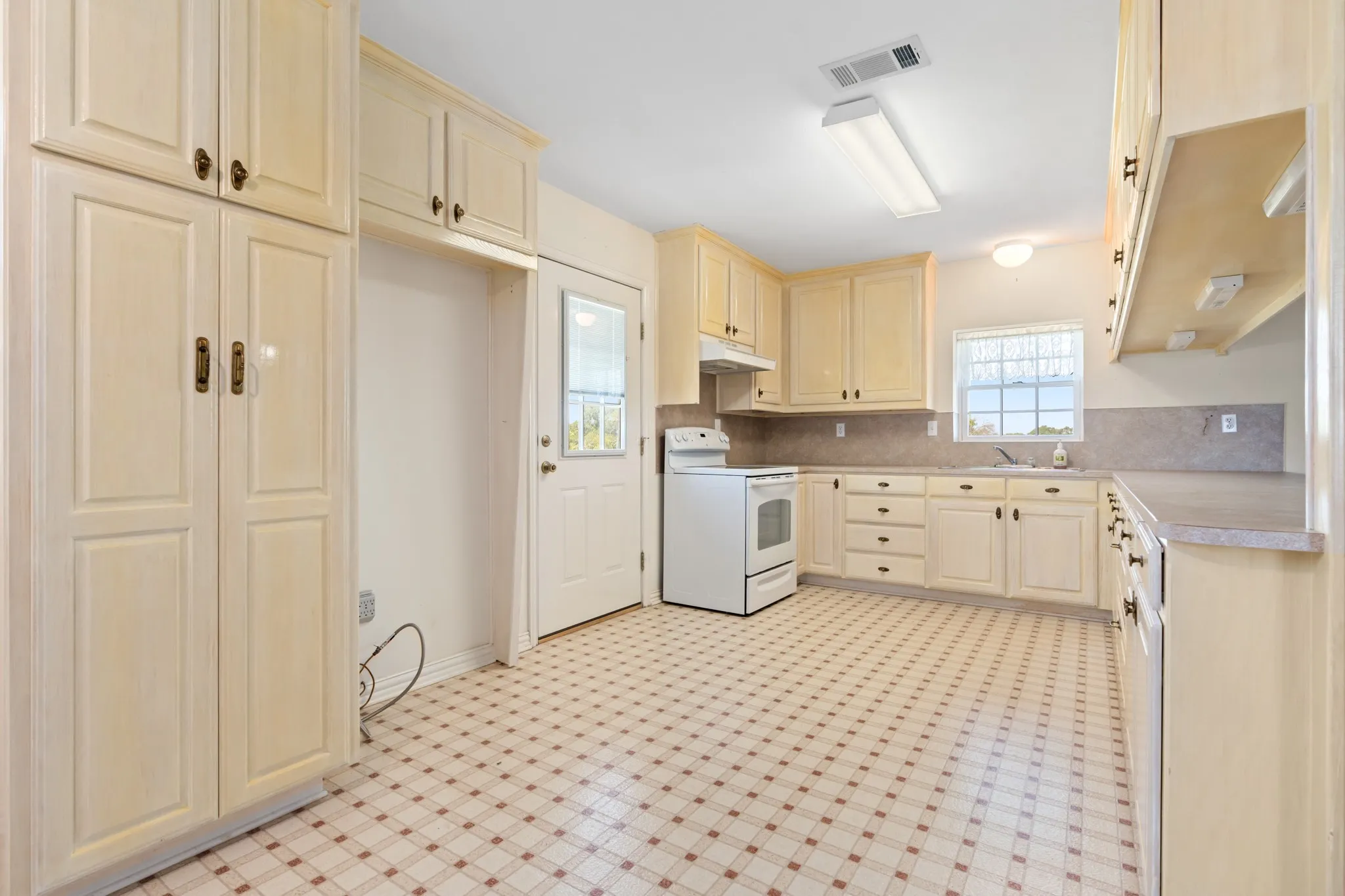 Kitchen featuring electric stove, light countertops, light floors, backsplash, and under cabinet range hood