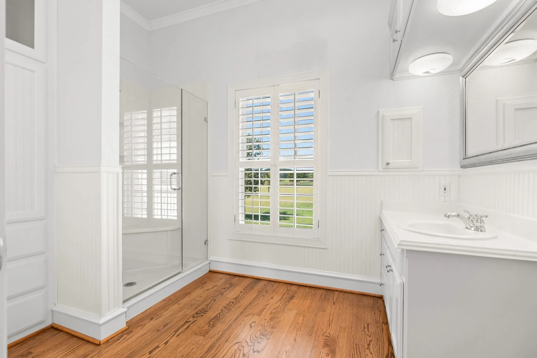 Bathroom with light wood-style floors, crown molding, a shower stall, vanity, and a wainscoted wall
