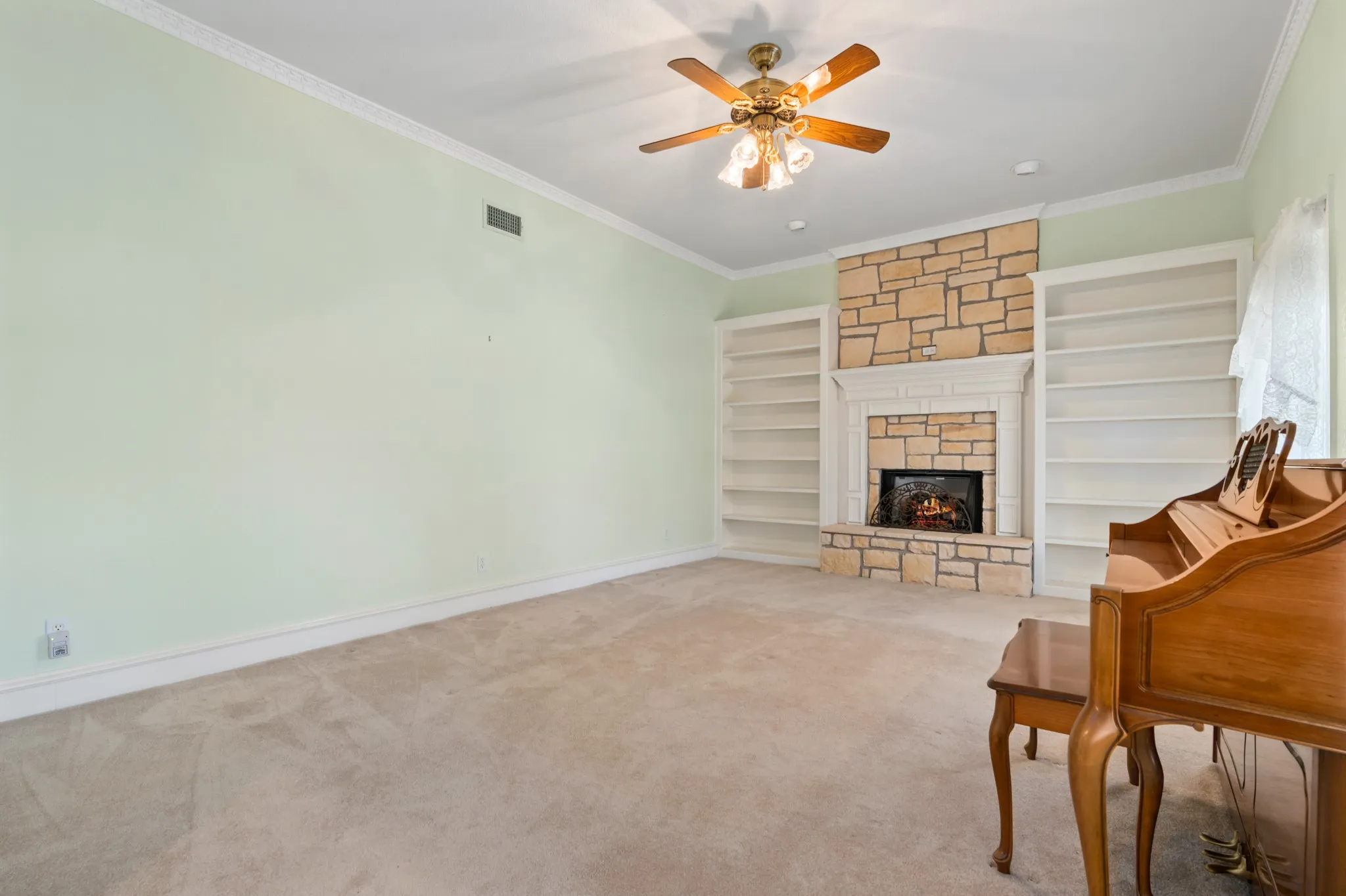 Living area with ornamental molding, a stone fireplace, carpet, built in features, and ceiling fan