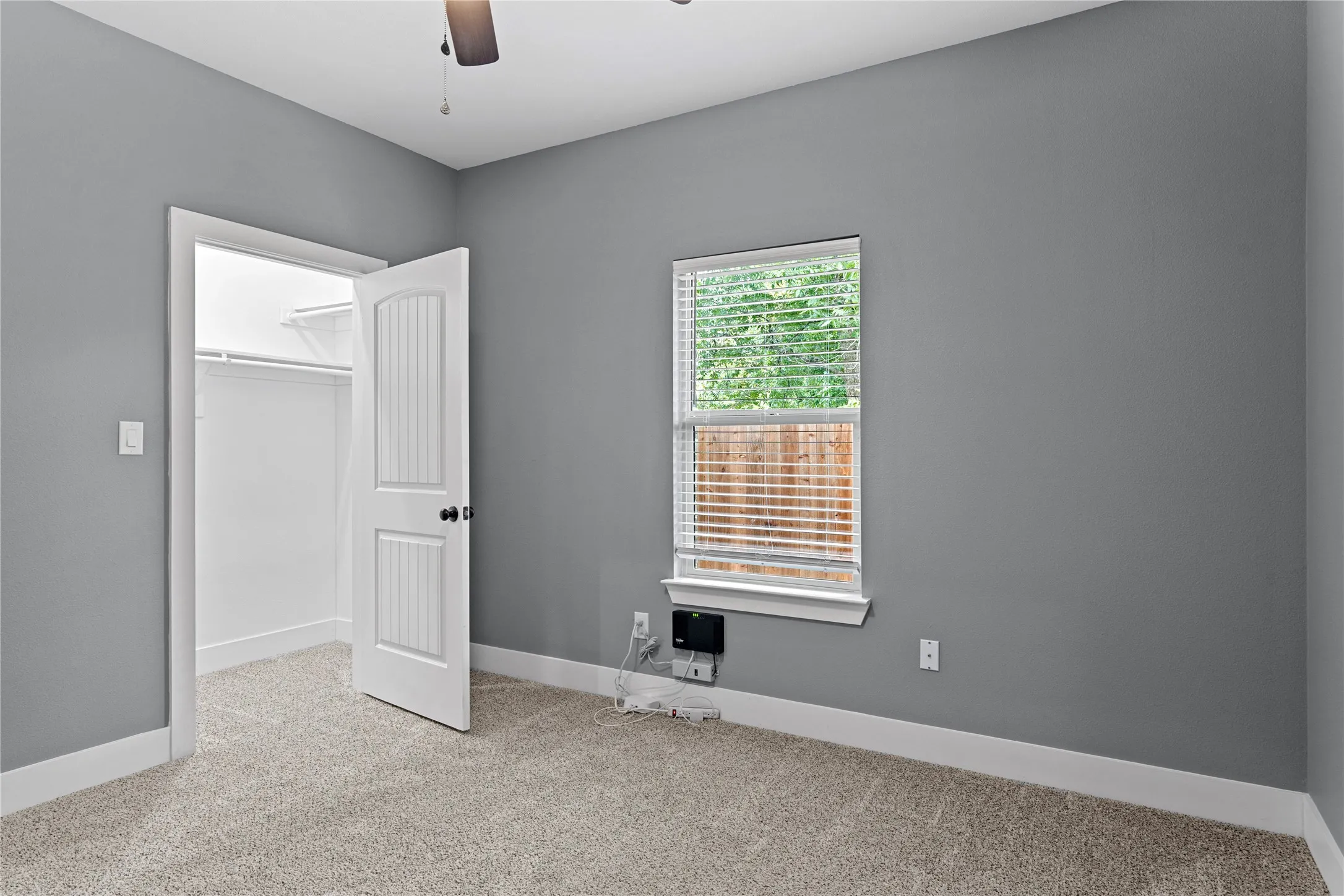 Unfurnished bedroom featuring light colored carpet, a walk in closet, and ceiling fan