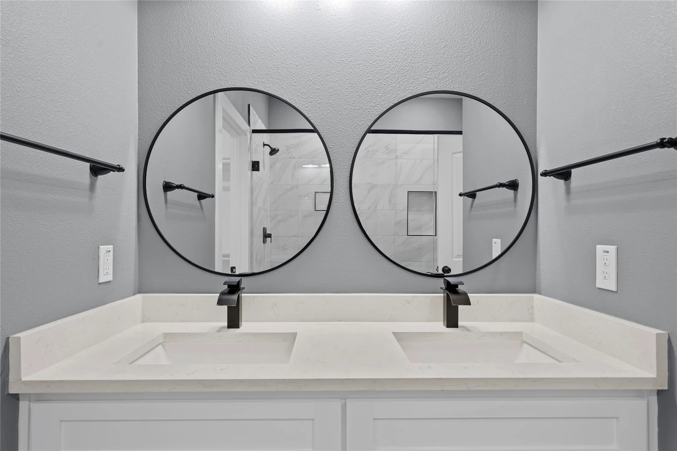 Bathroom with a textured wall, a stall shower, and double vanity