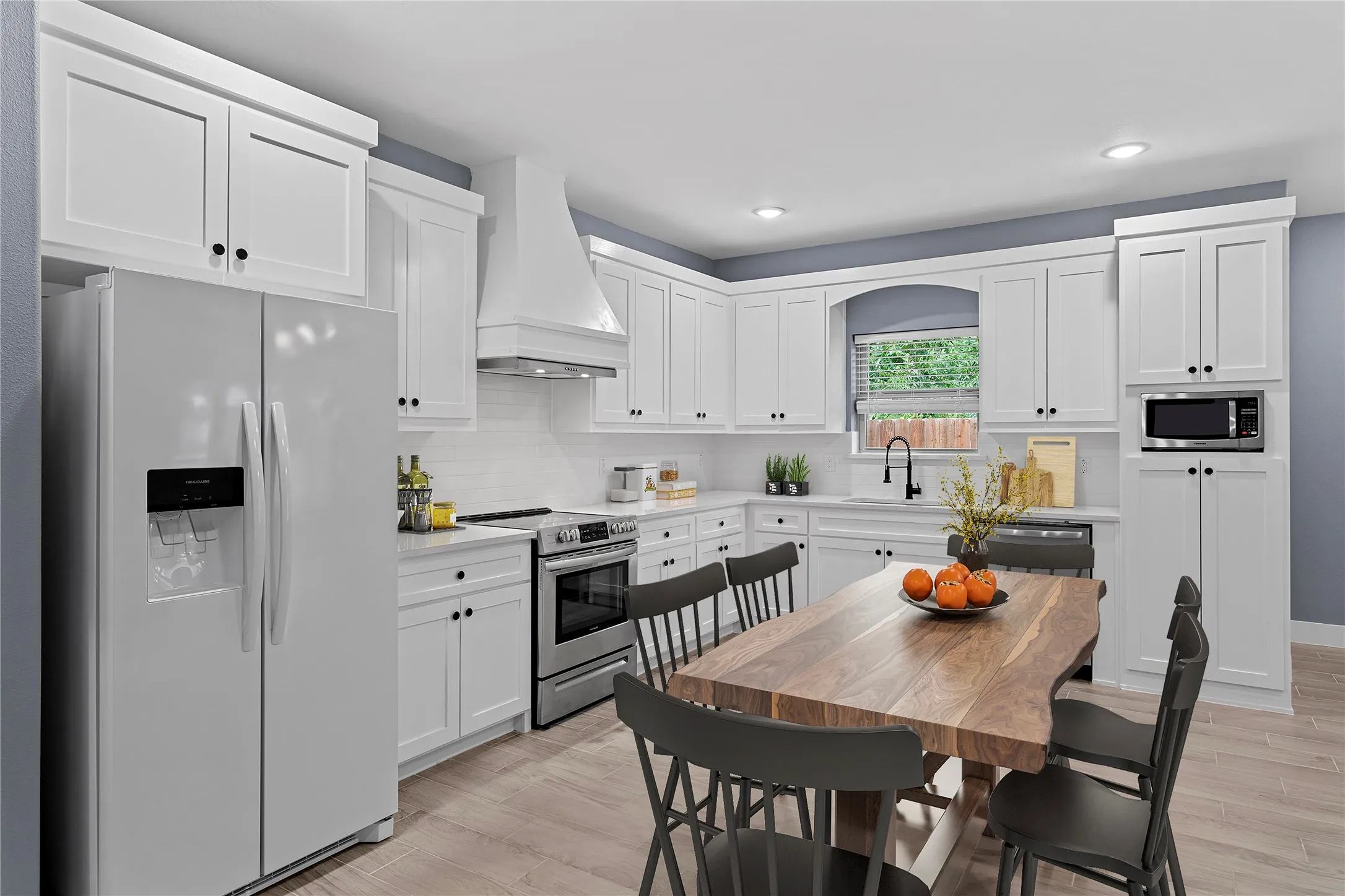 Kitchen featuring appliances with stainless steel finishes, premium range hood, white cabinets, and recessed lighting