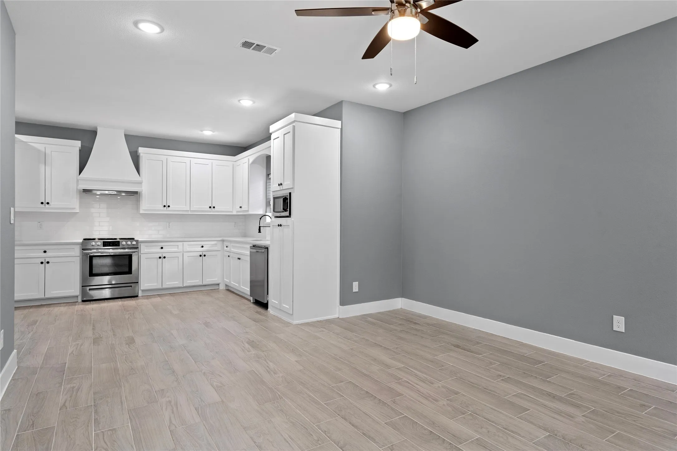 Kitchen featuring white cabinets, backsplash, light countertops, light wood-type flooring, and recessed lighting