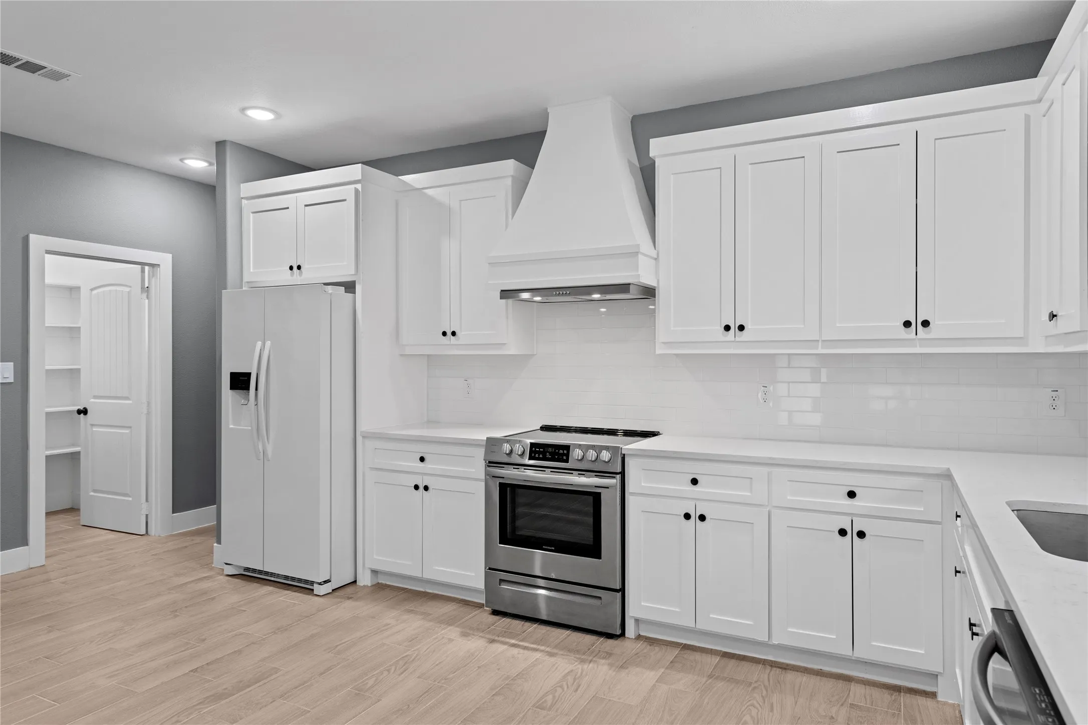 Kitchen with white refrigerator with ice dispenser, custom range hood, stainless steel electric range, white cabinetry, and recessed lighting