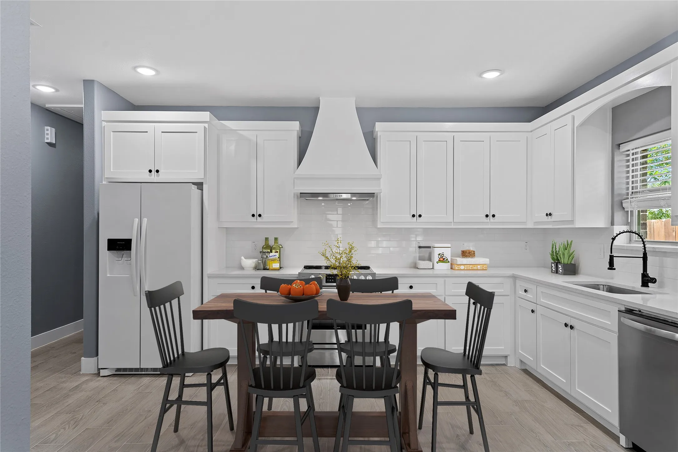 Kitchen featuring stainless steel appliances, backsplash, white cabinetry, custom range hood, and light wood-style floors