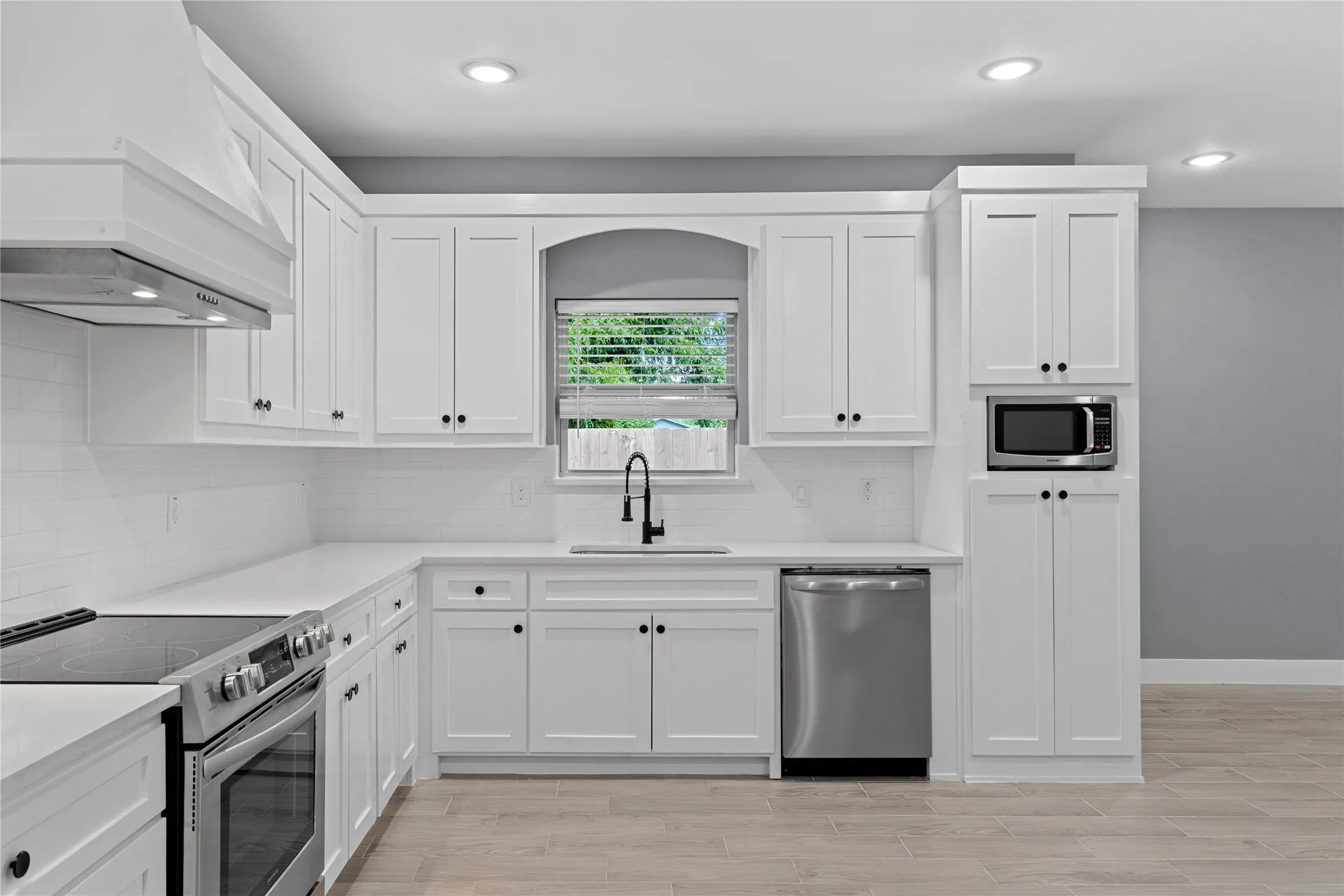 Kitchen featuring stainless steel appliances, white cabinets, custom exhaust hood, decorative backsplash, and recessed lighting