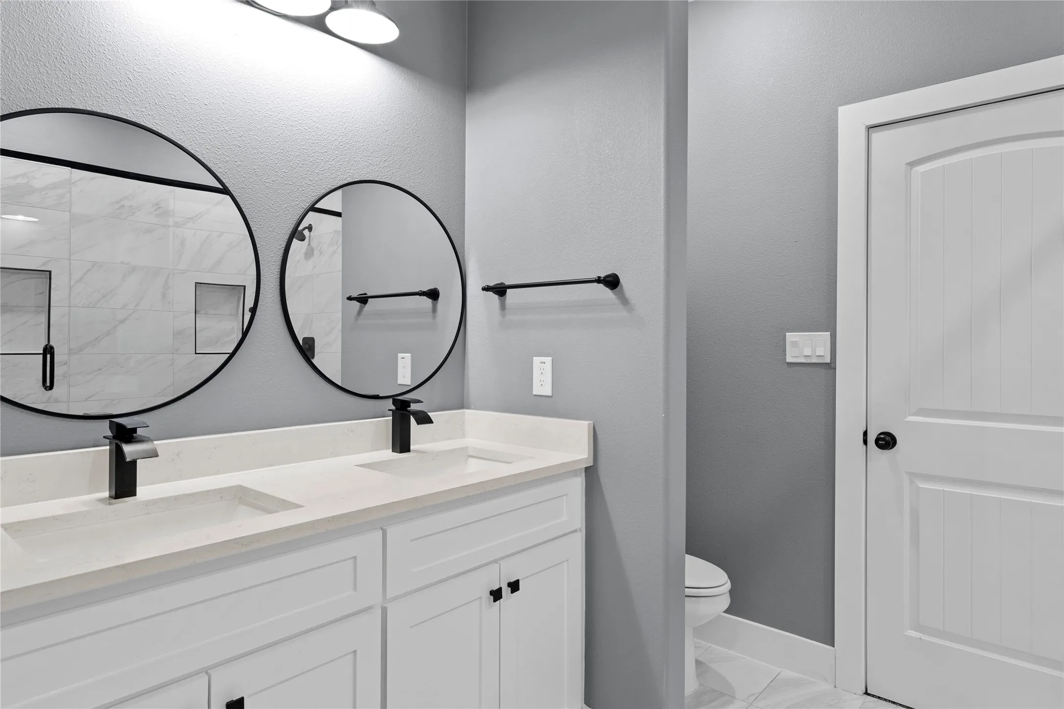Full bath featuring double vanity, light marble finish flooring, a stall shower, and a textured wall