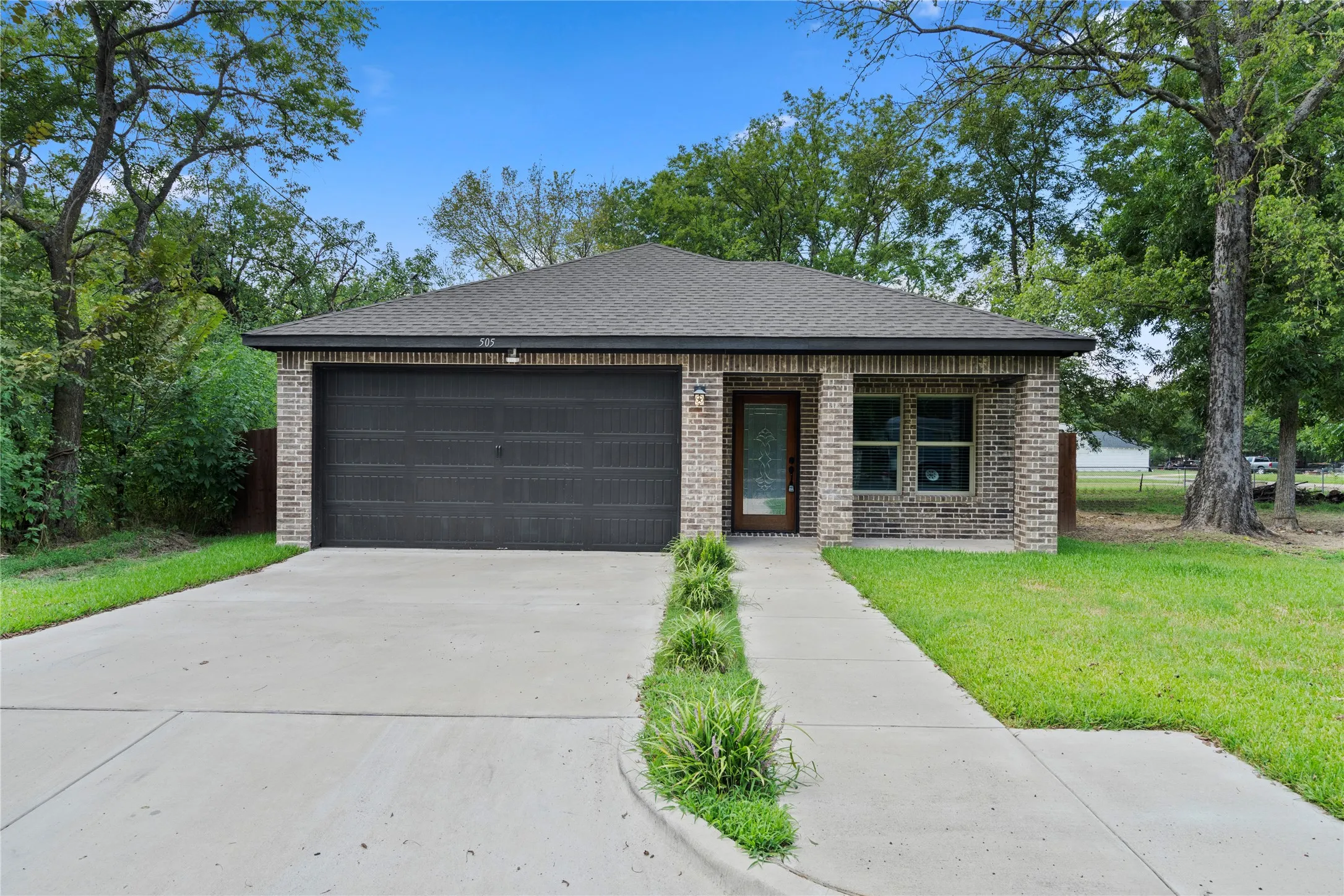 View of front of house with brick siding, roof with shingles, driveway, and a front yard
