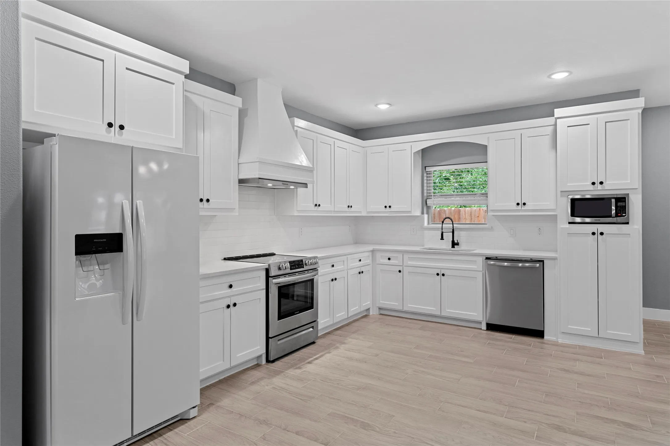 Kitchen featuring stainless steel appliances, custom exhaust hood, white cabinets, decorative backsplash, and recessed lighting