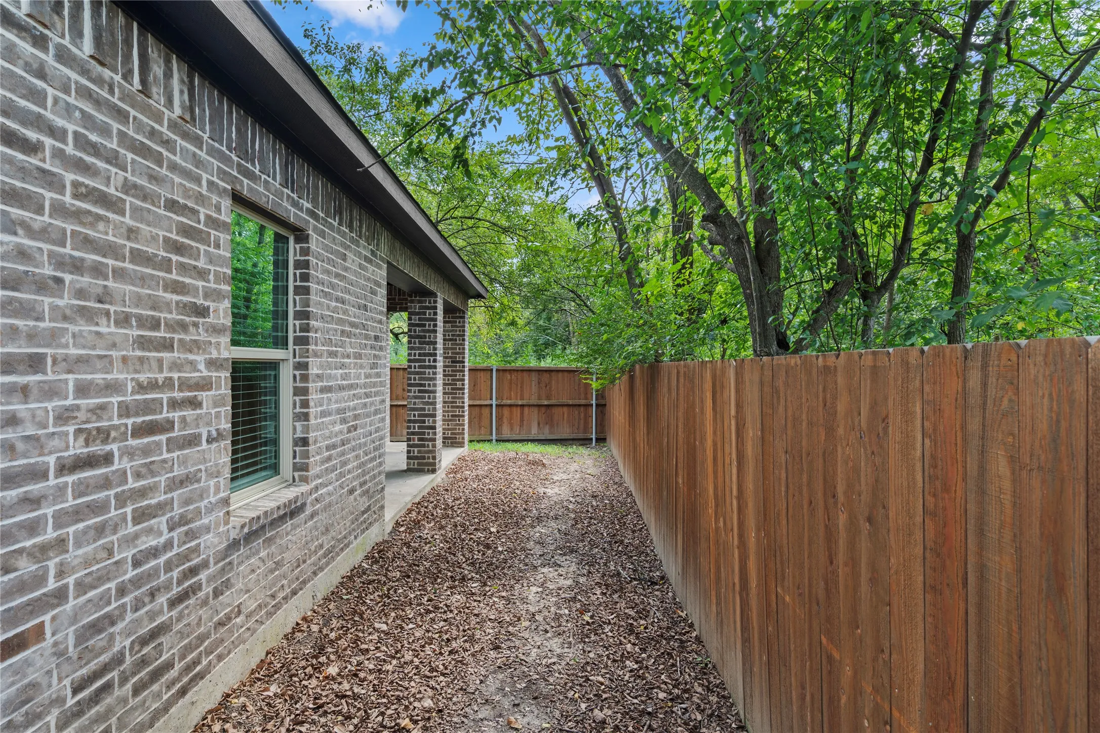 View of side of property with brick siding, a fenced backyard, and a patio