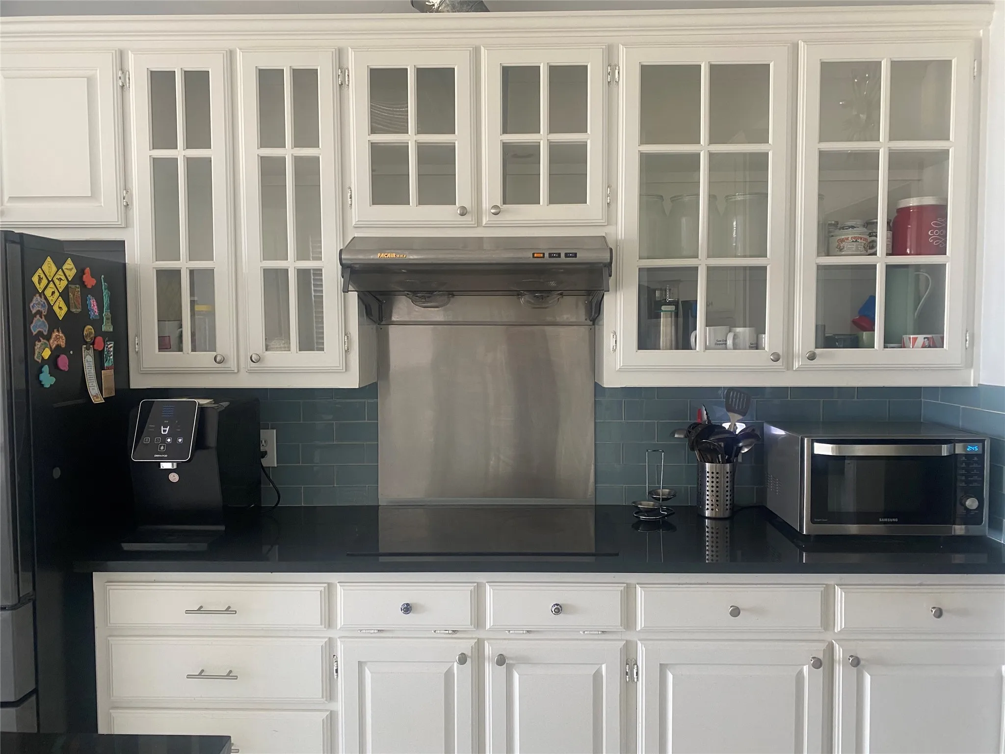Kitchen featuring white cabinetry, tasteful backsplash, freestanding refrigerator, glass insert cabinets, and stainless steel microwave