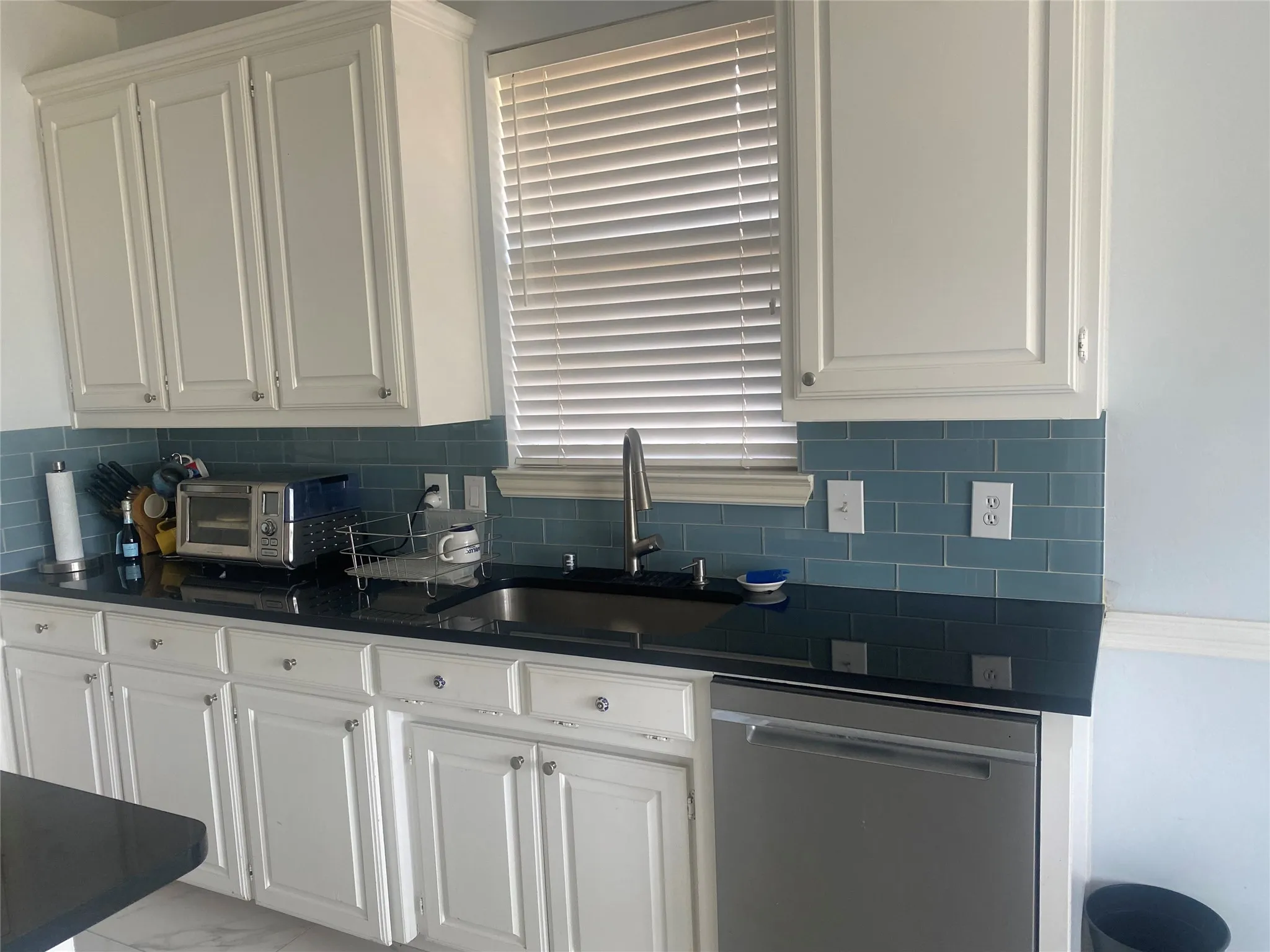 Kitchen with white cabinetry, dishwasher, tasteful backsplash, dark stone countertops, and light marble finish floors