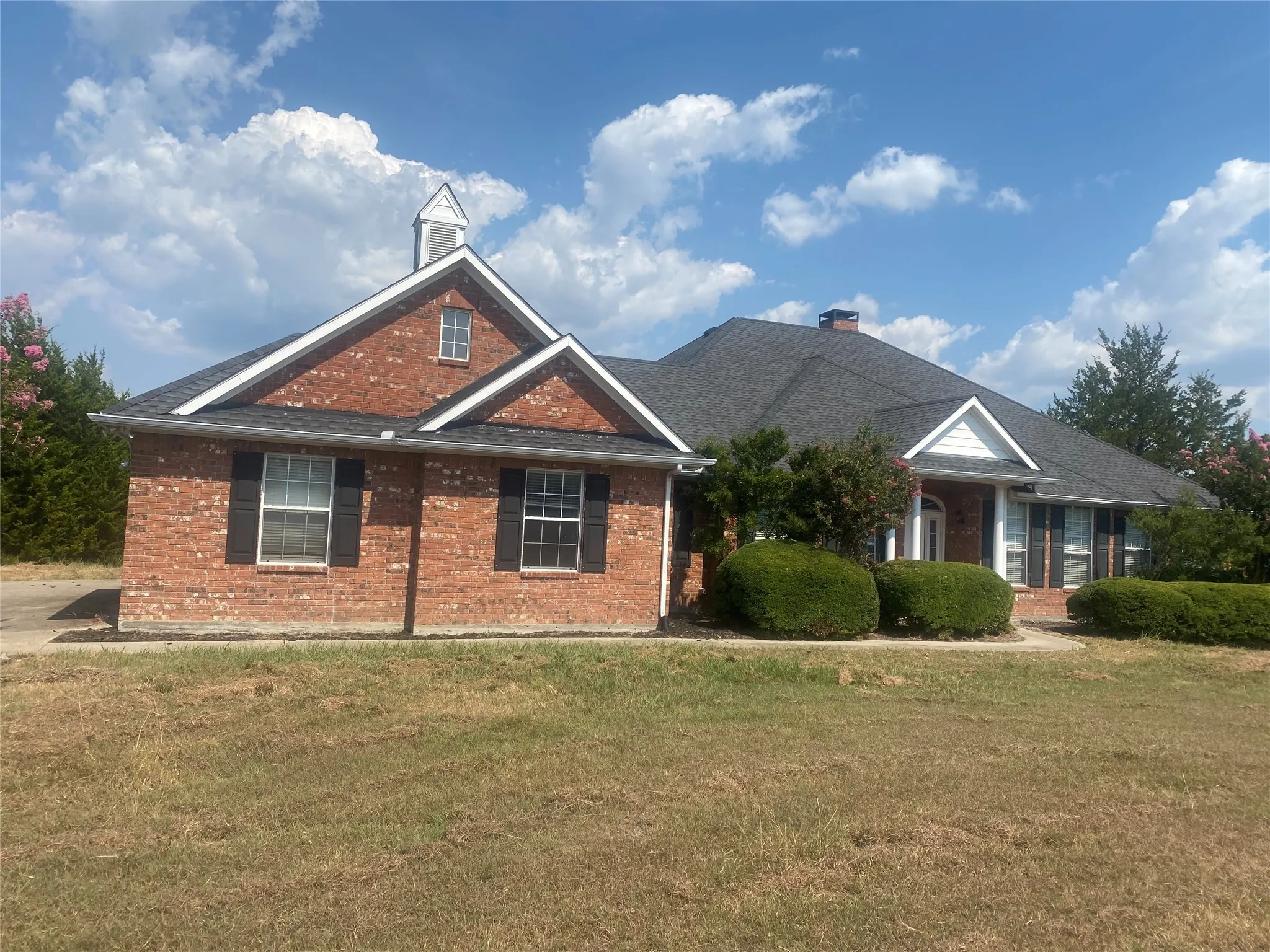 View of front of home featuring a front lawn, a chimney, brick siding, and roof with shingles