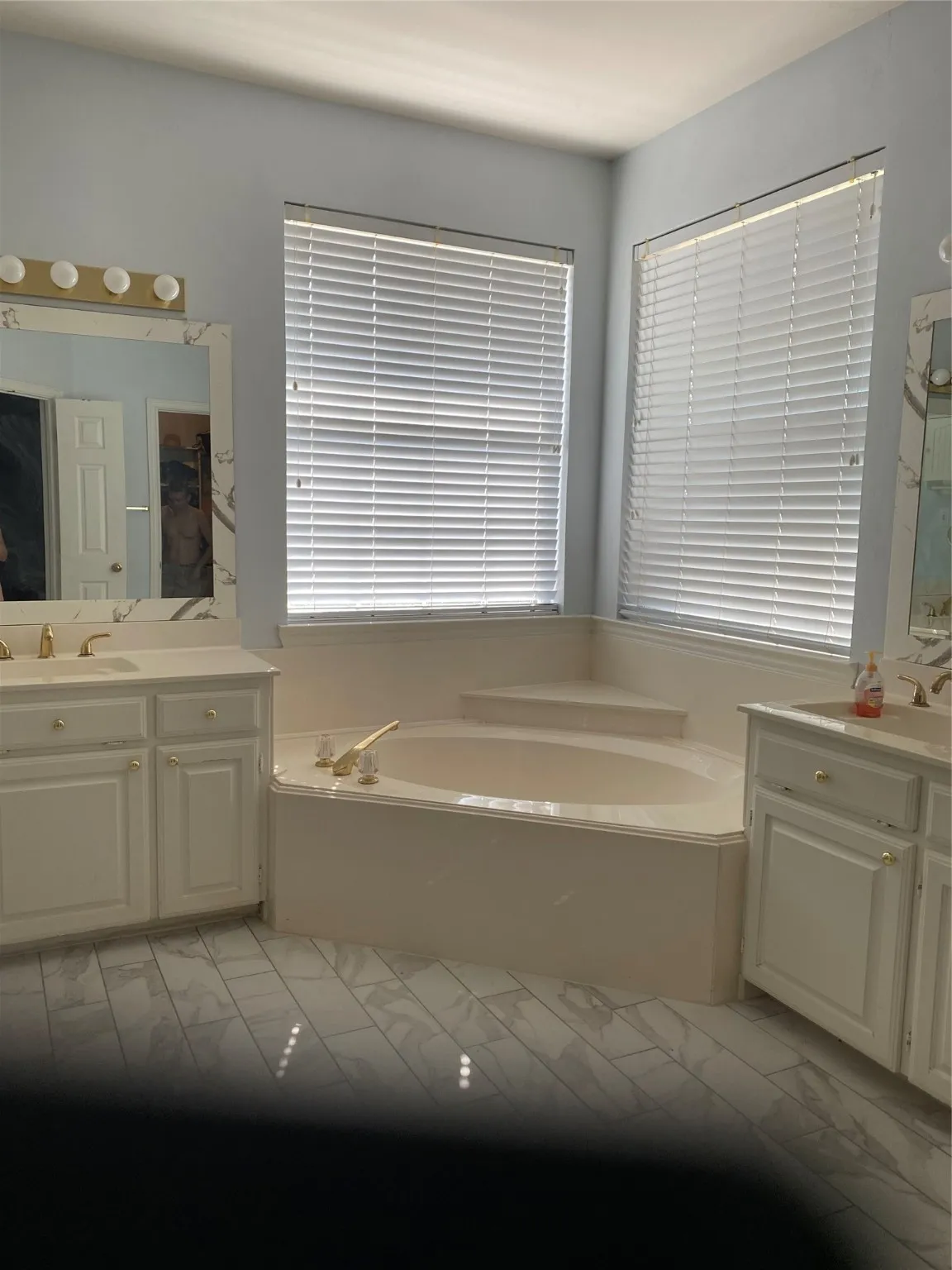 Full bathroom with two vanities, a bath, and light marble finish floors