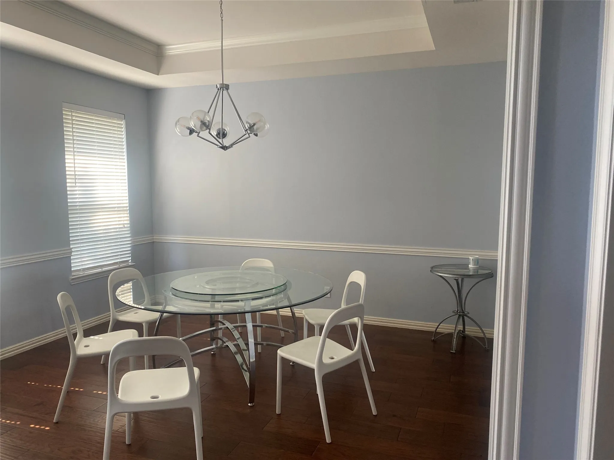 Dining area with dark wood-type flooring, a raised ceiling, crown molding, and a chandelier