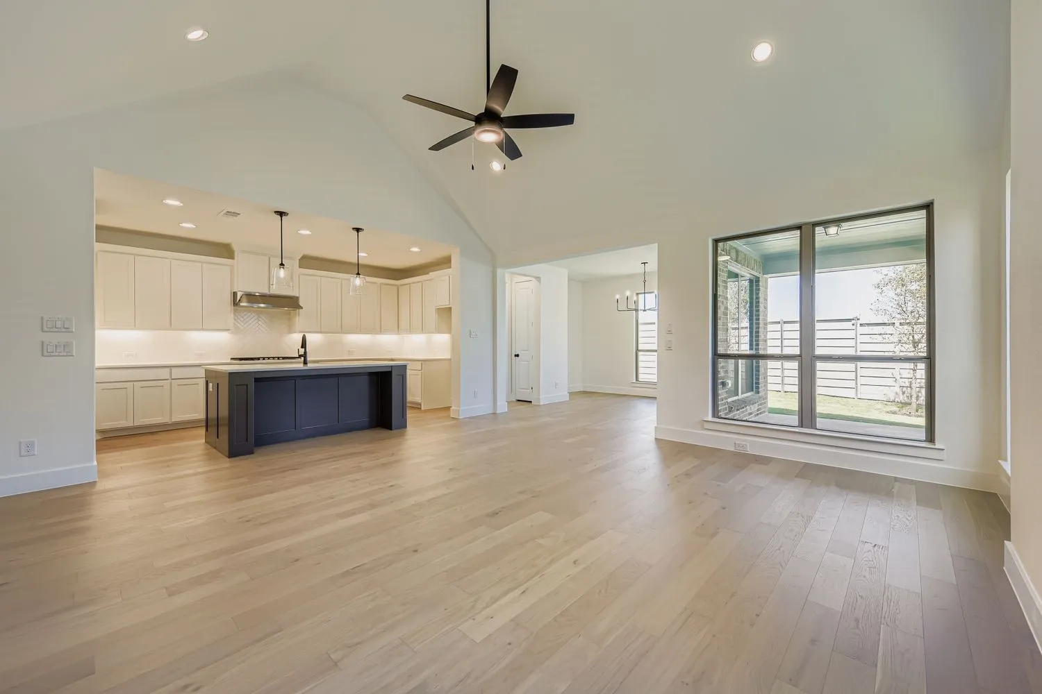 Unfurnished living room featuring high vaulted ceiling, ceiling fan, light wood finished floors, recessed lighting, and a chandelier