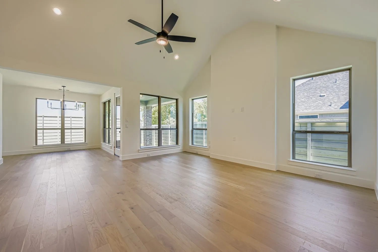 Unfurnished living room featuring recessed lighting, light wood-type flooring, high vaulted ceiling, a ceiling fan, and a chandelier