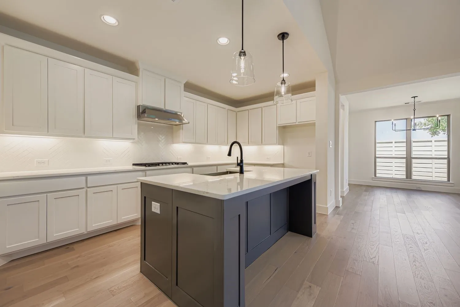 Kitchen featuring white cabinetry, decorative backsplash, decorative light fixtures, light stone counters, and light wood-style flooring