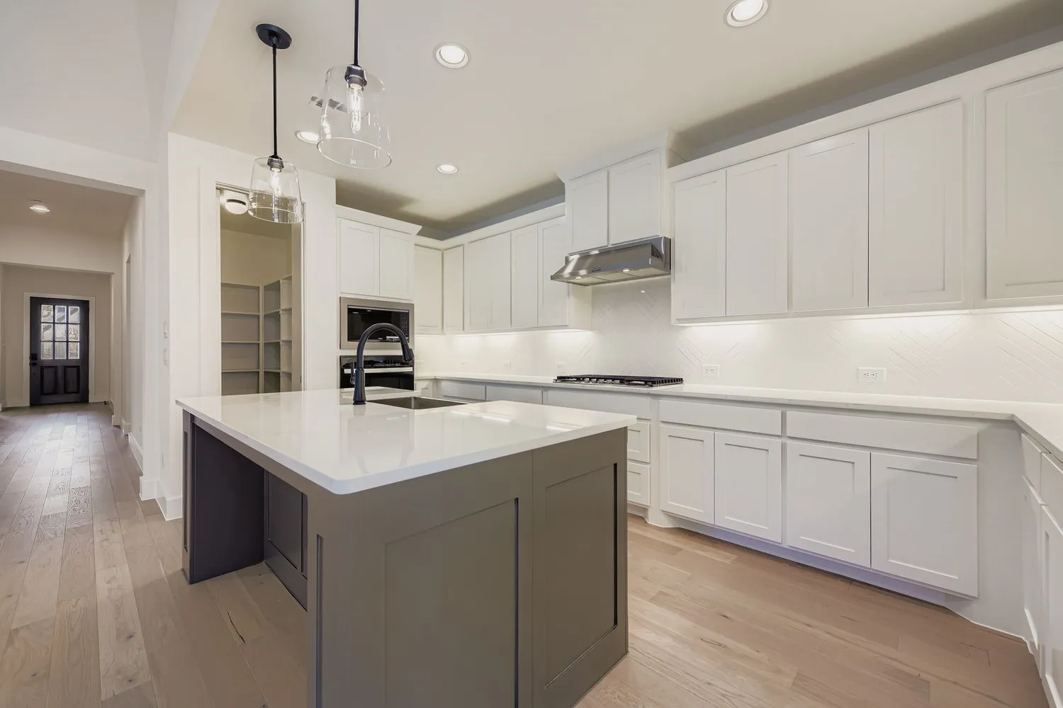 Kitchen with white cabinetry, tasteful backsplash, light wood-style floors, a center island with sink, and recessed lighting