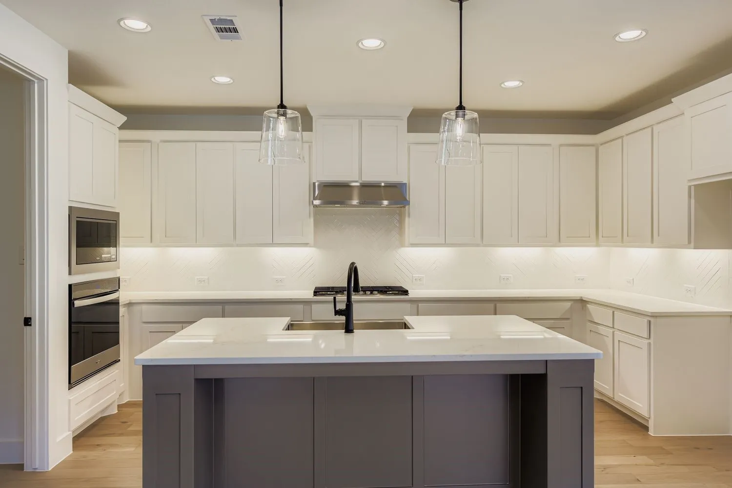 Kitchen with white cabinets, a kitchen island with sink, light wood finished floors, decorative backsplash, and recessed lighting