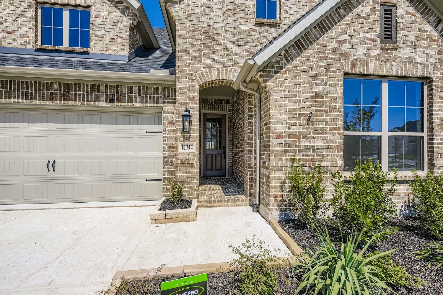 Property entrance with brick siding, a garage, roof with shingles, and concrete driveway