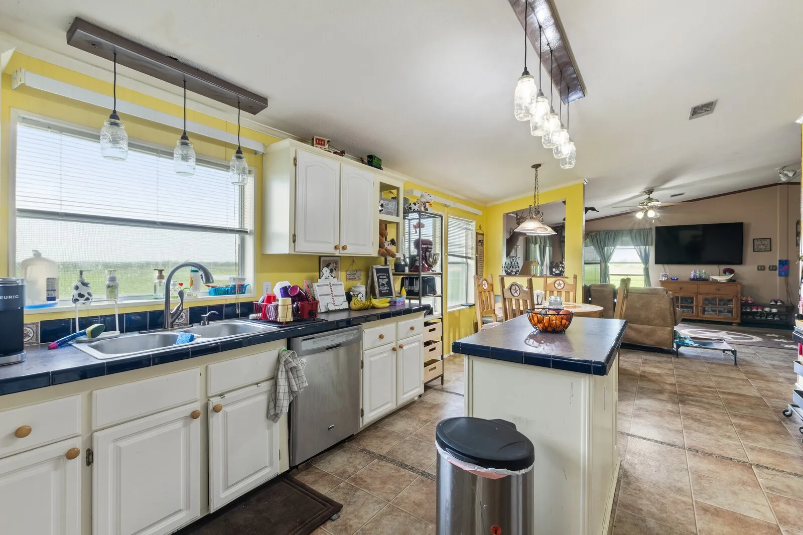 Kitchen with tile countertops, open floor plan, white cabinetry, stainless steel dishwasher, and crown molding