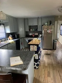 Kitchen featuring stainless steel fridge, a breakfast bar area, light wood finished floors, gray cabinetry, and range with electric stovetop