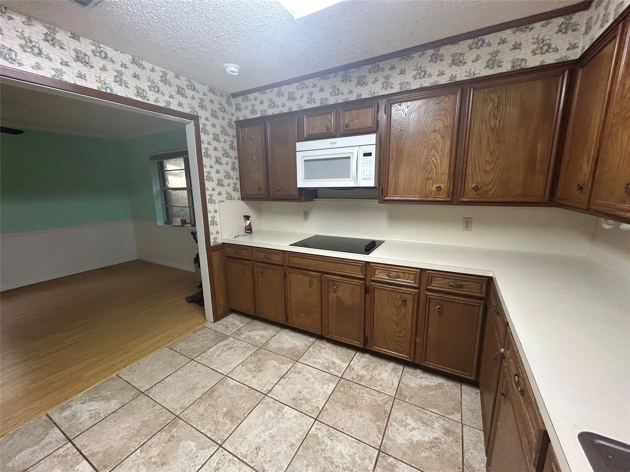Kitchen with a textured ceiling, light countertops, light tile patterned floors, white microwave, and dark brown cabinetry